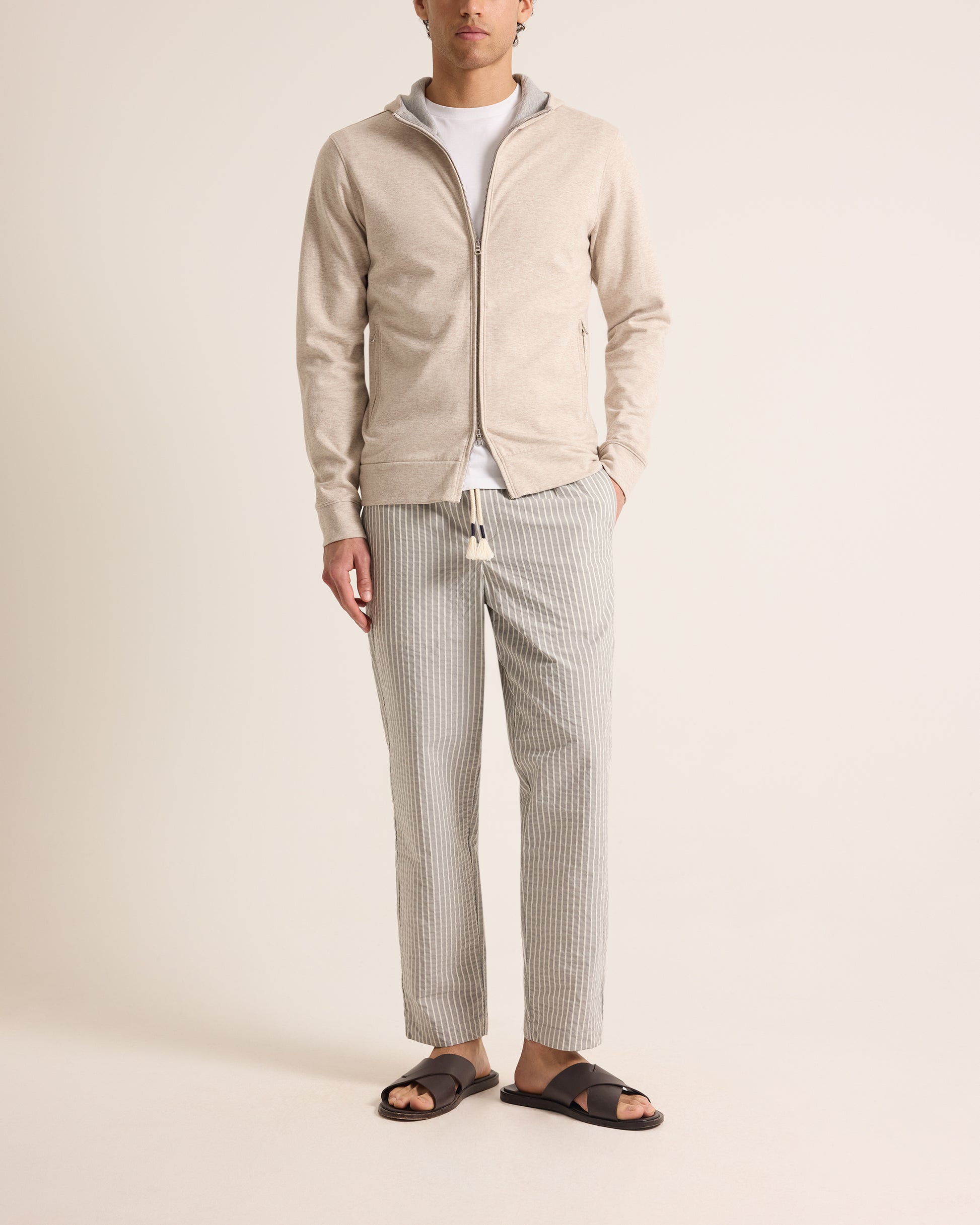 Man wearing a beige zip-up jacket, white shirt, and gray checkered pants on a plain background