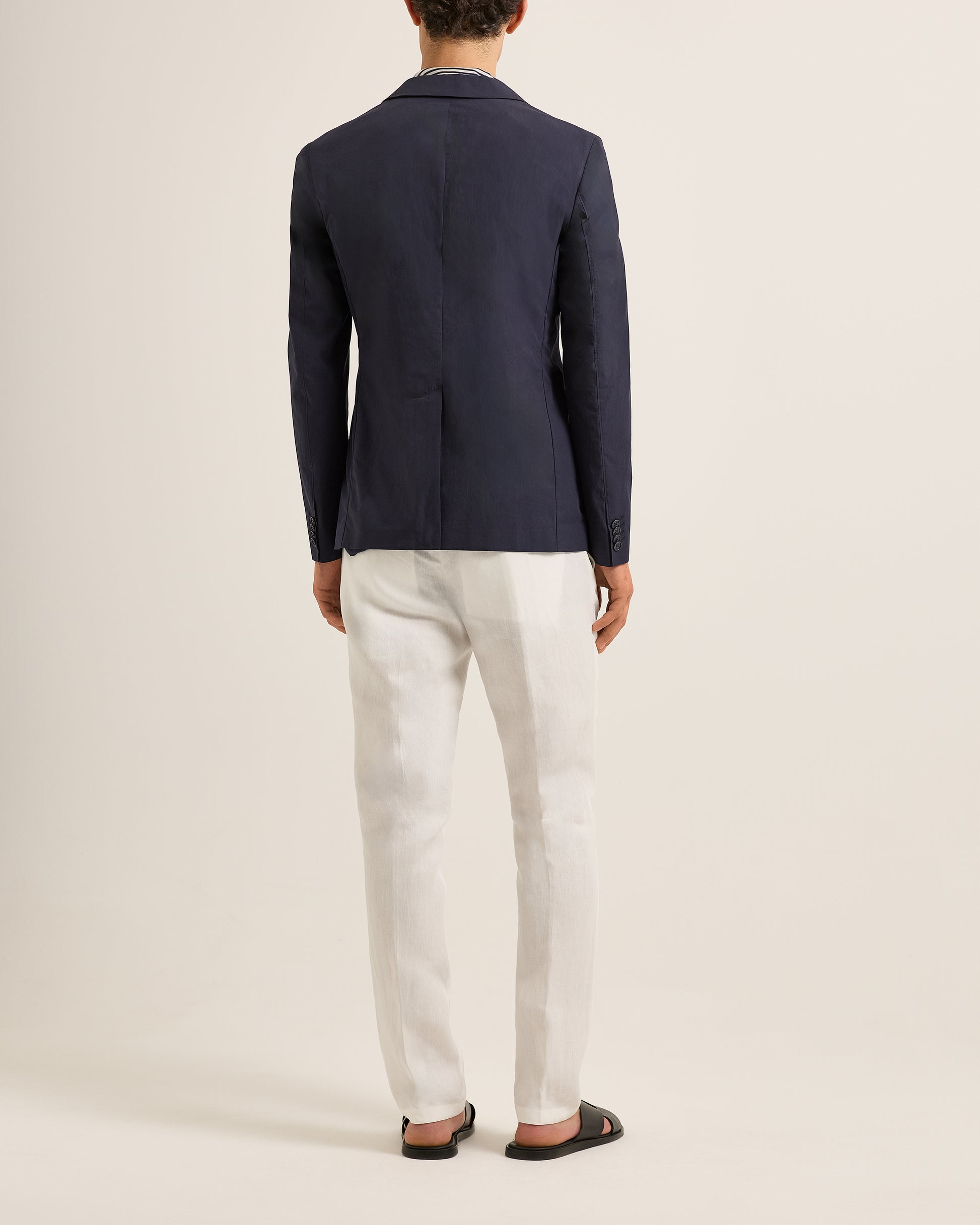 Person wearing a navy blazer and white pants on a light beige background