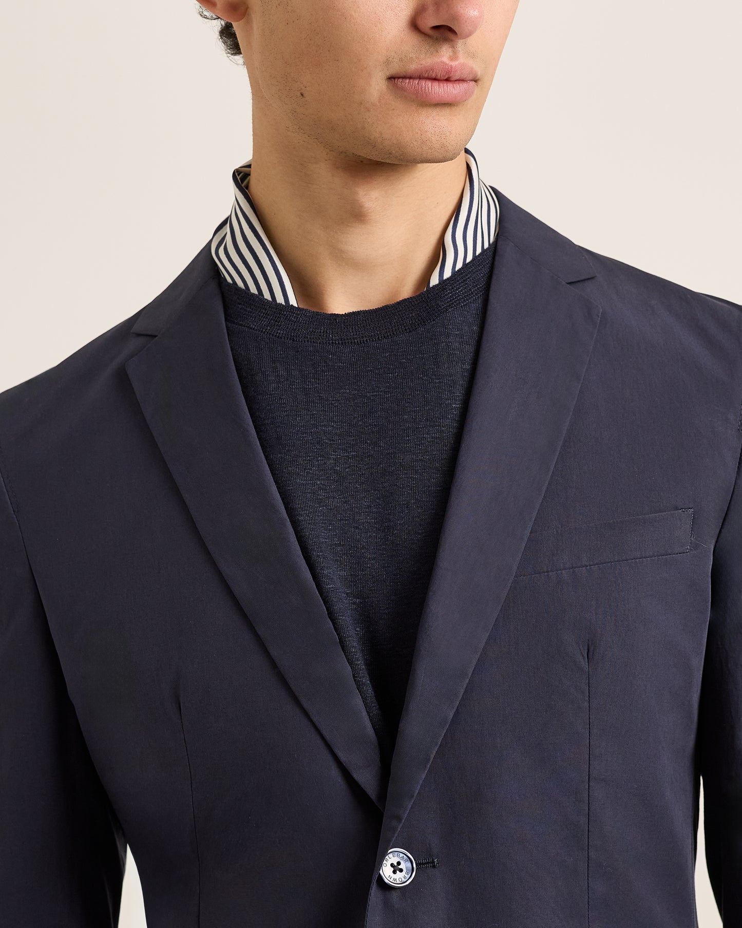 Man wearing a navy blazer over a striped shirt on a beige background