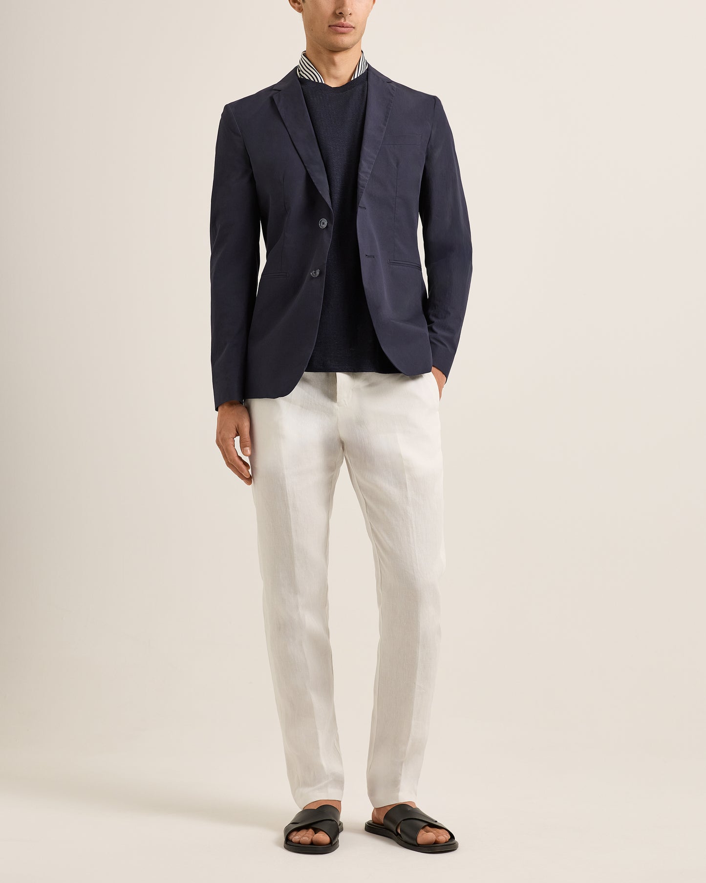 Person wearing a navy blazer over a striped shirt with white pants on a plain background