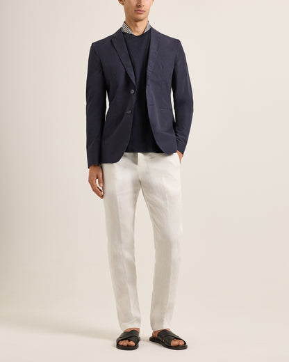 Person wearing a navy blazer over a striped shirt with white pants on a plain background