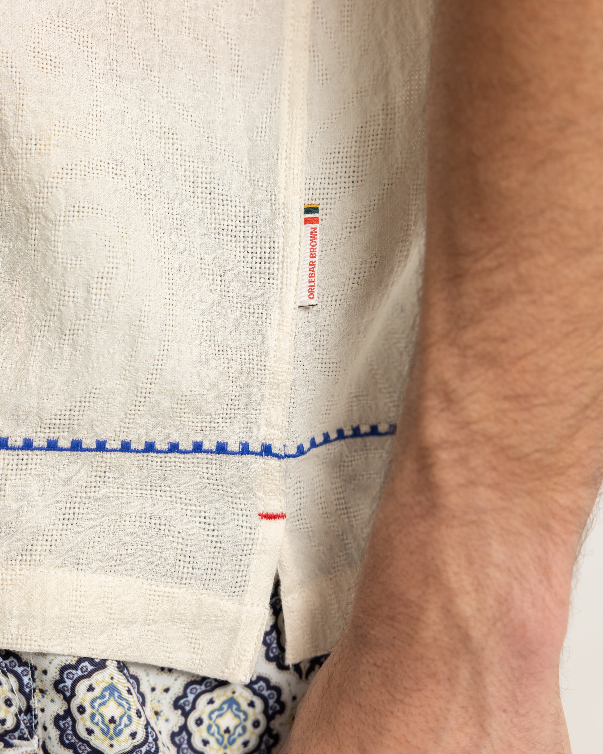 Closeup of white linen shirt with blue embroidery detail and brand logo tag