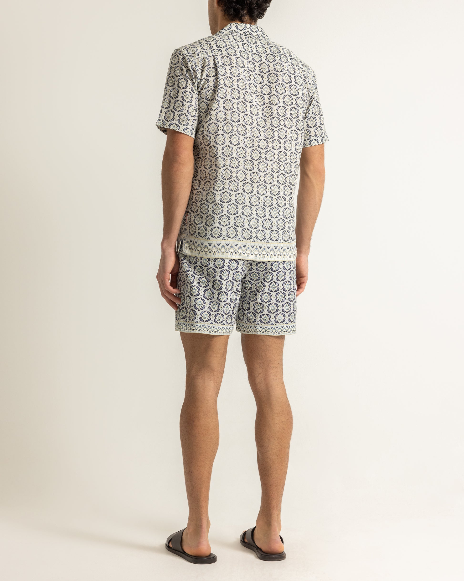Man wearing printed beige shirt and swim shorts on a plain background