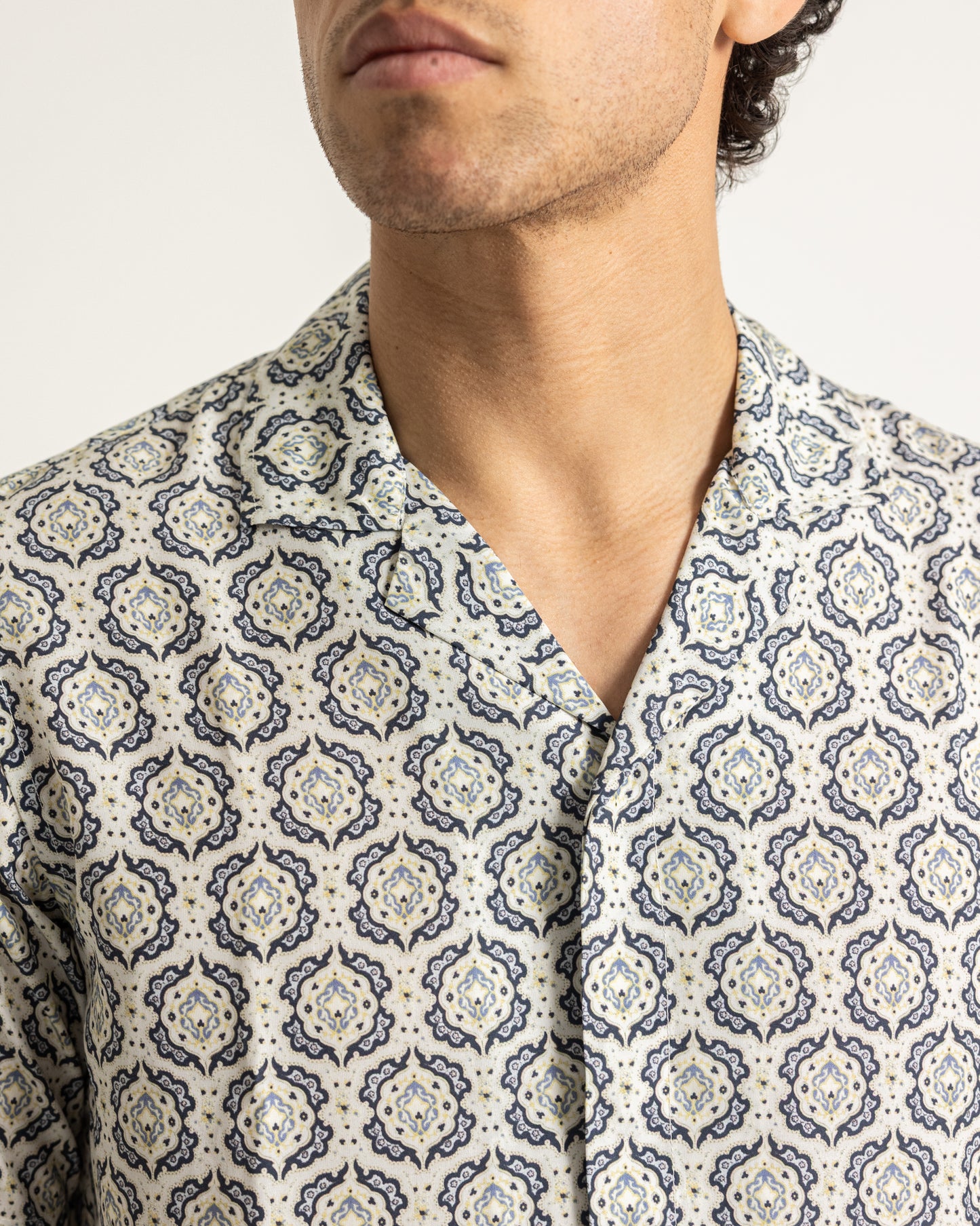 Man wearing a patterned shirt with a neutral background