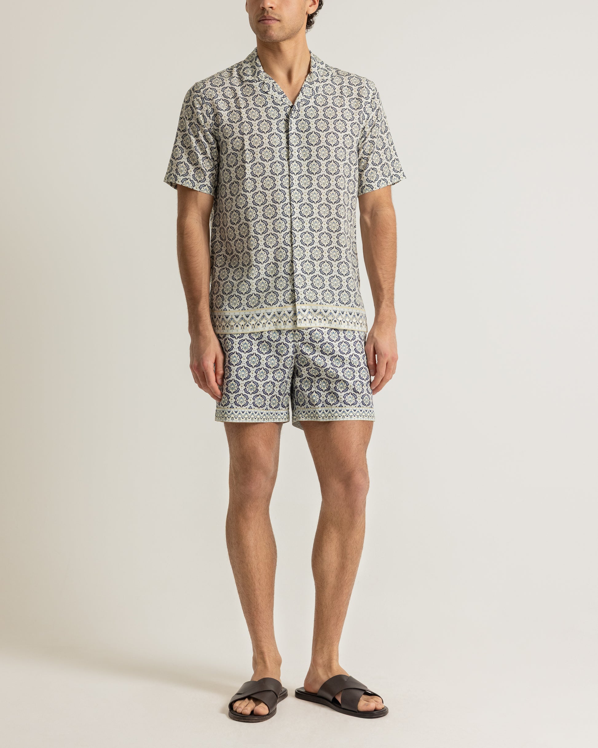 Man wearing printed beige shirt and swim shorts on a plain background