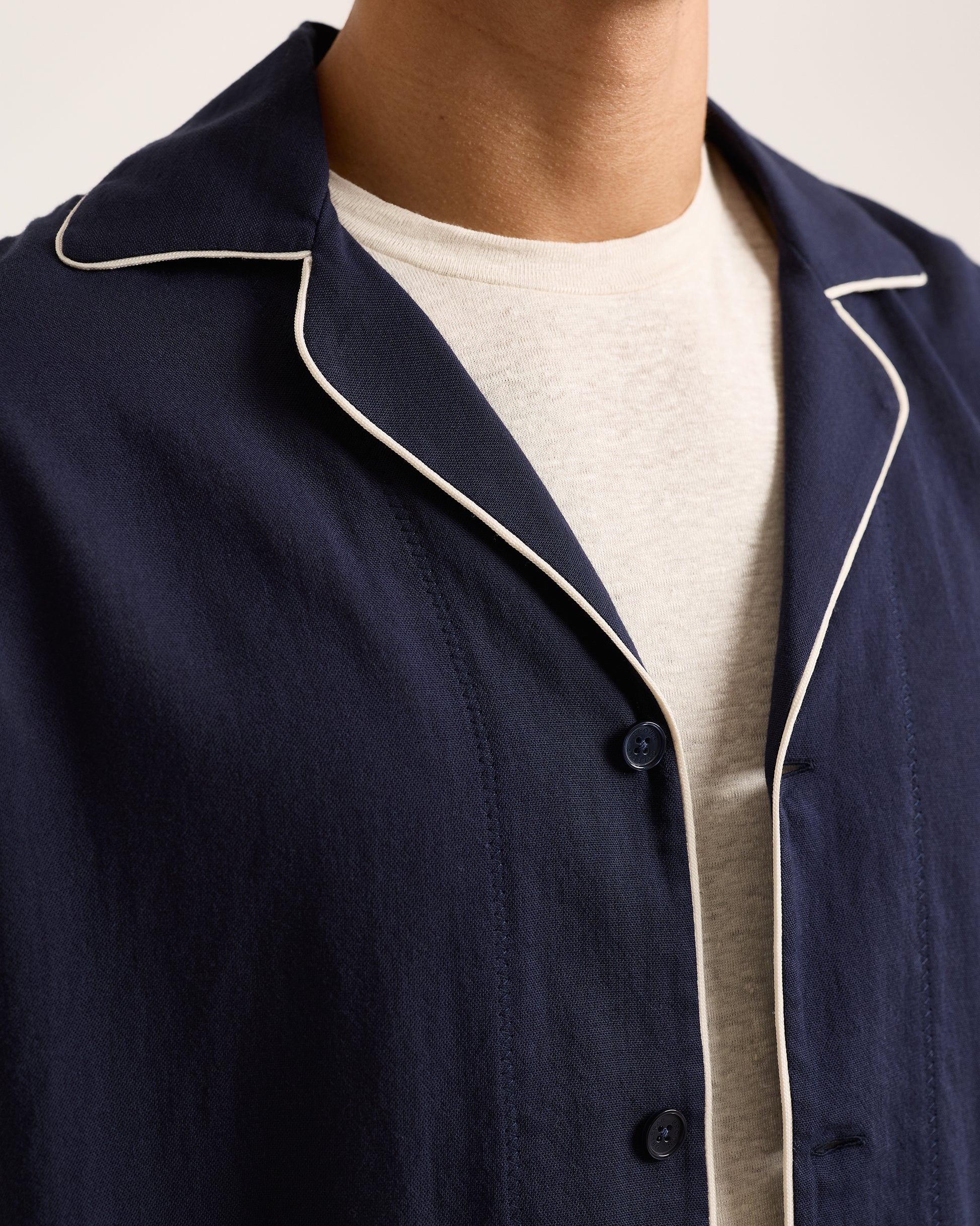 Navy blue pajama top with white piping on a neutral background