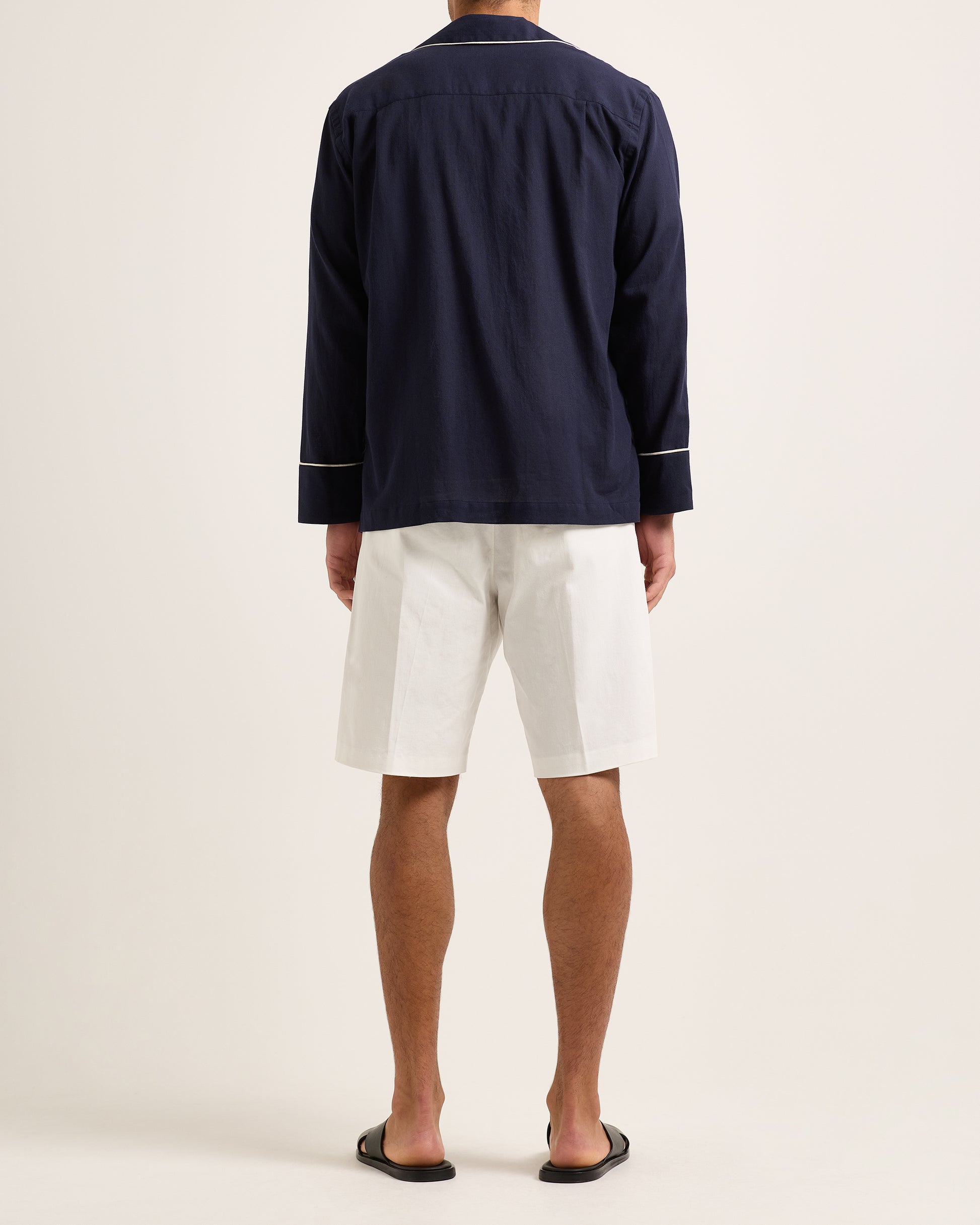 Person wearing a navy jacket with white trim, white shirt, and white shorts on a plain background