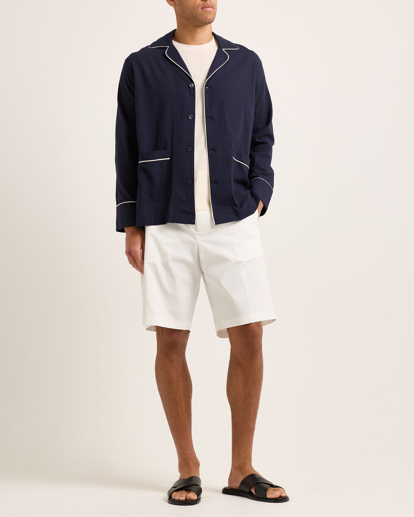 Person wearing a navy jacket with white trim, white shirt, and white shorts on a plain background