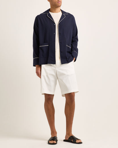 Person wearing a navy jacket with white trim, white shirt, and white shorts on a plain background
