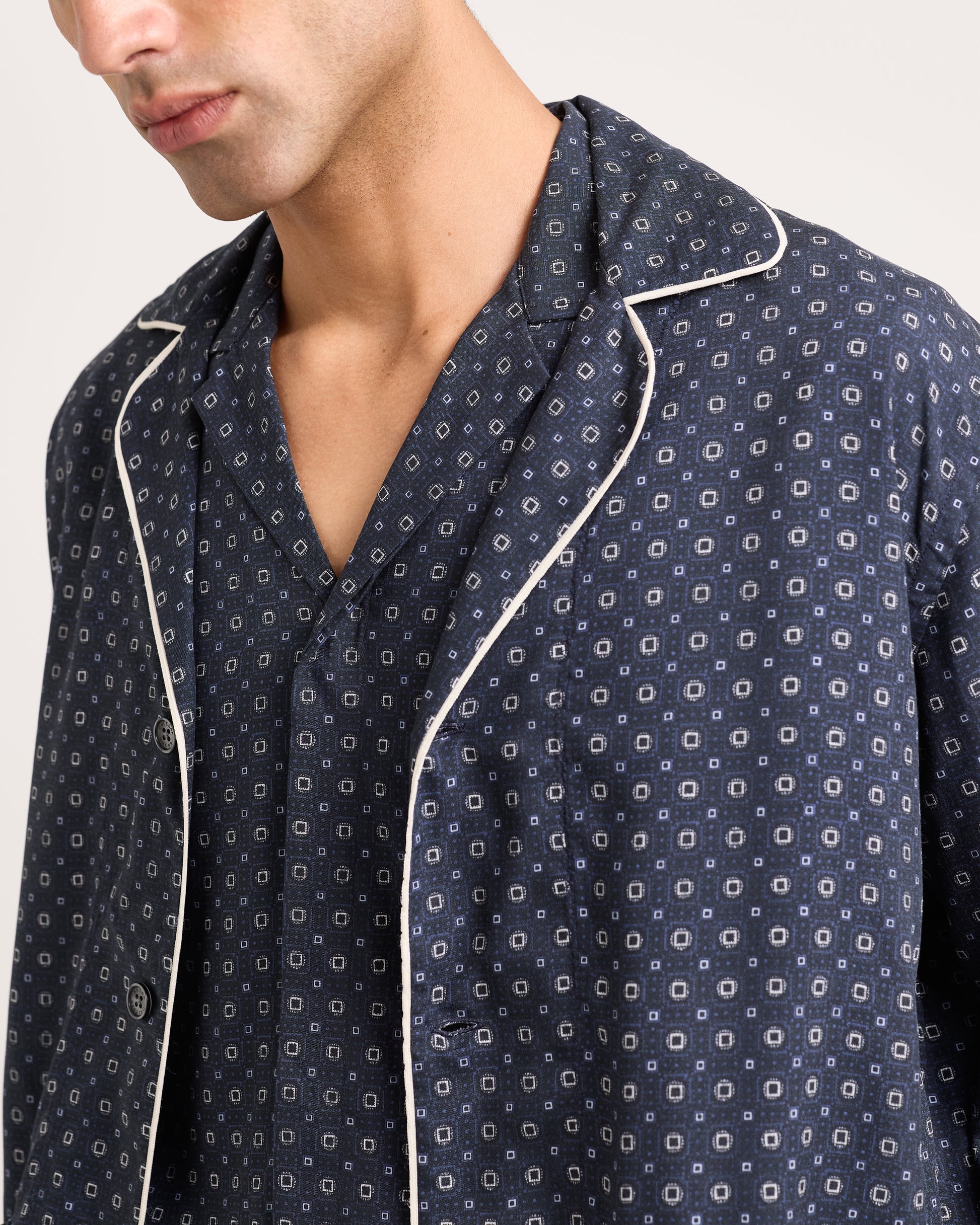 Man wearing a navy patterned shirt with white piping on a plain background