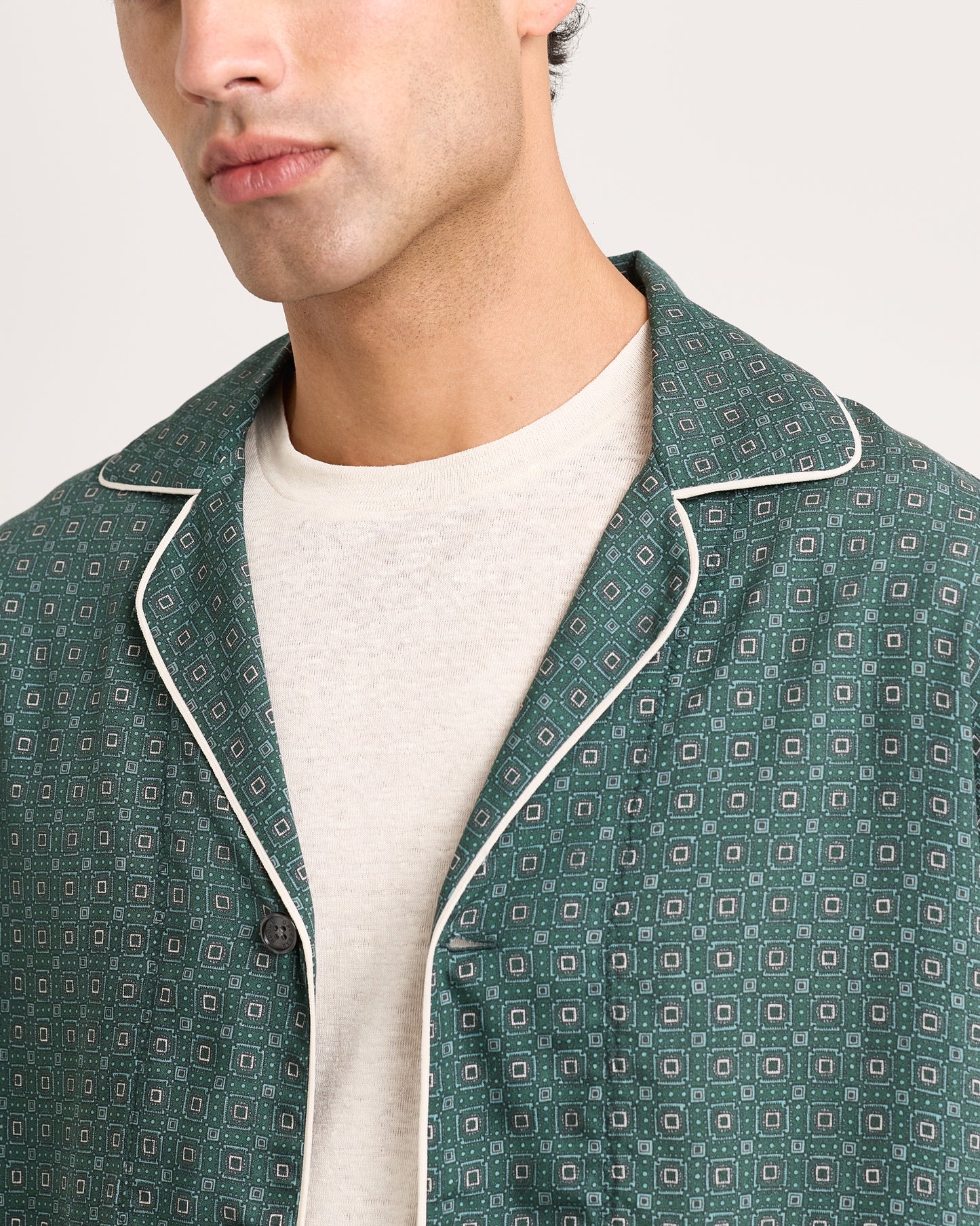 Close-up of green patterned jacket with white piping on a white background