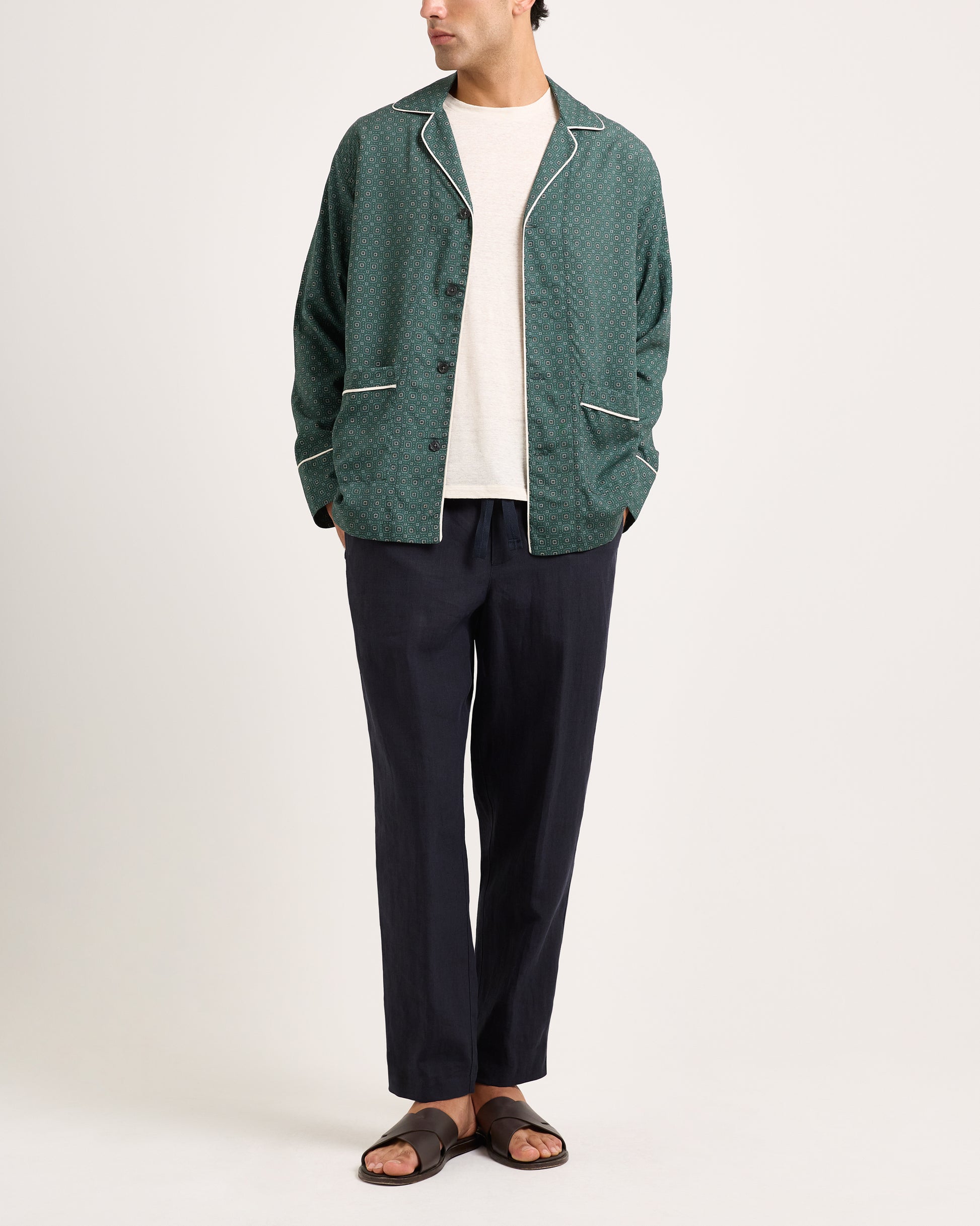 Person wearing a green patterned jacket and dark pants on a white background