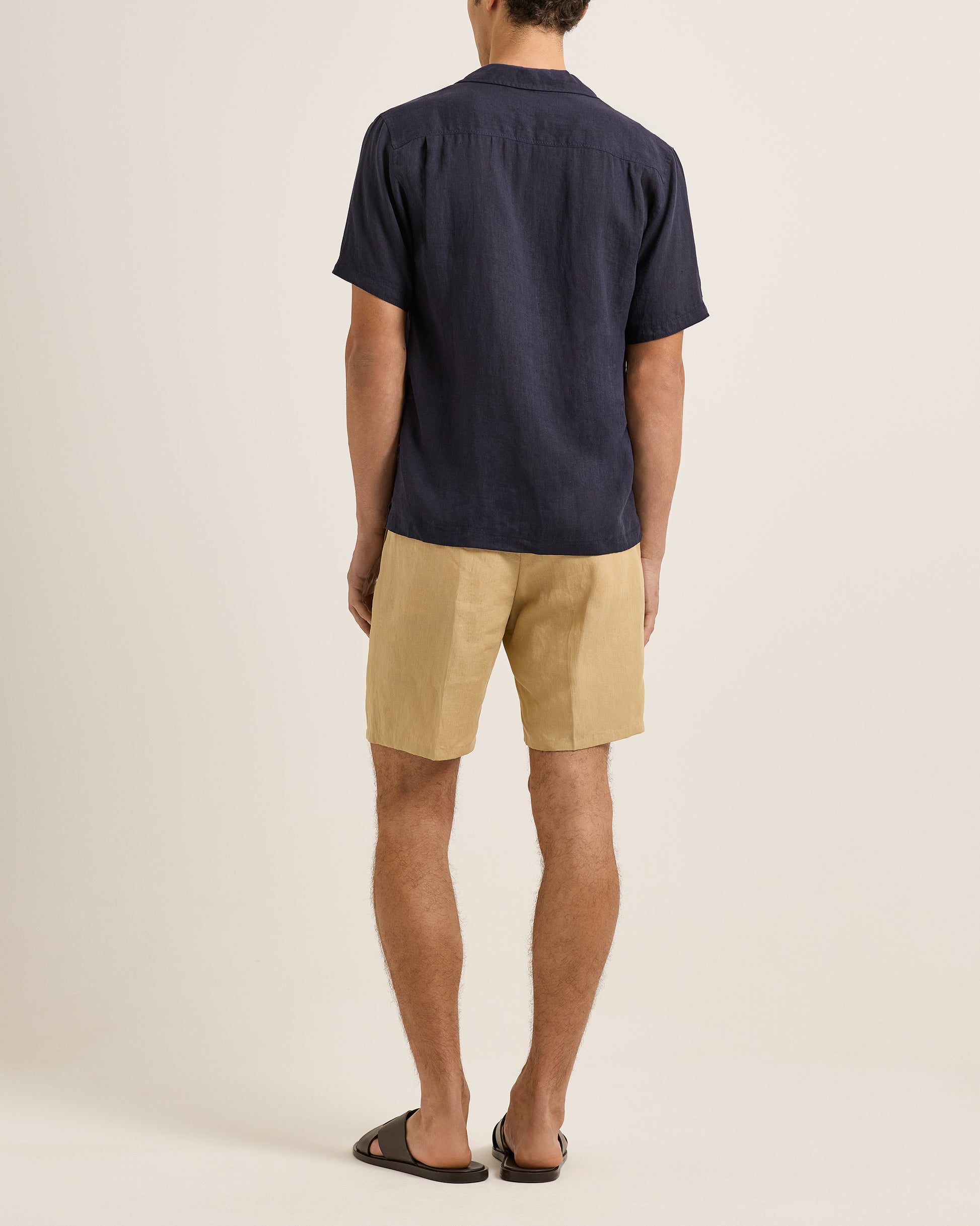 Person wearing a navy shirt and beige shorts on a plain background
