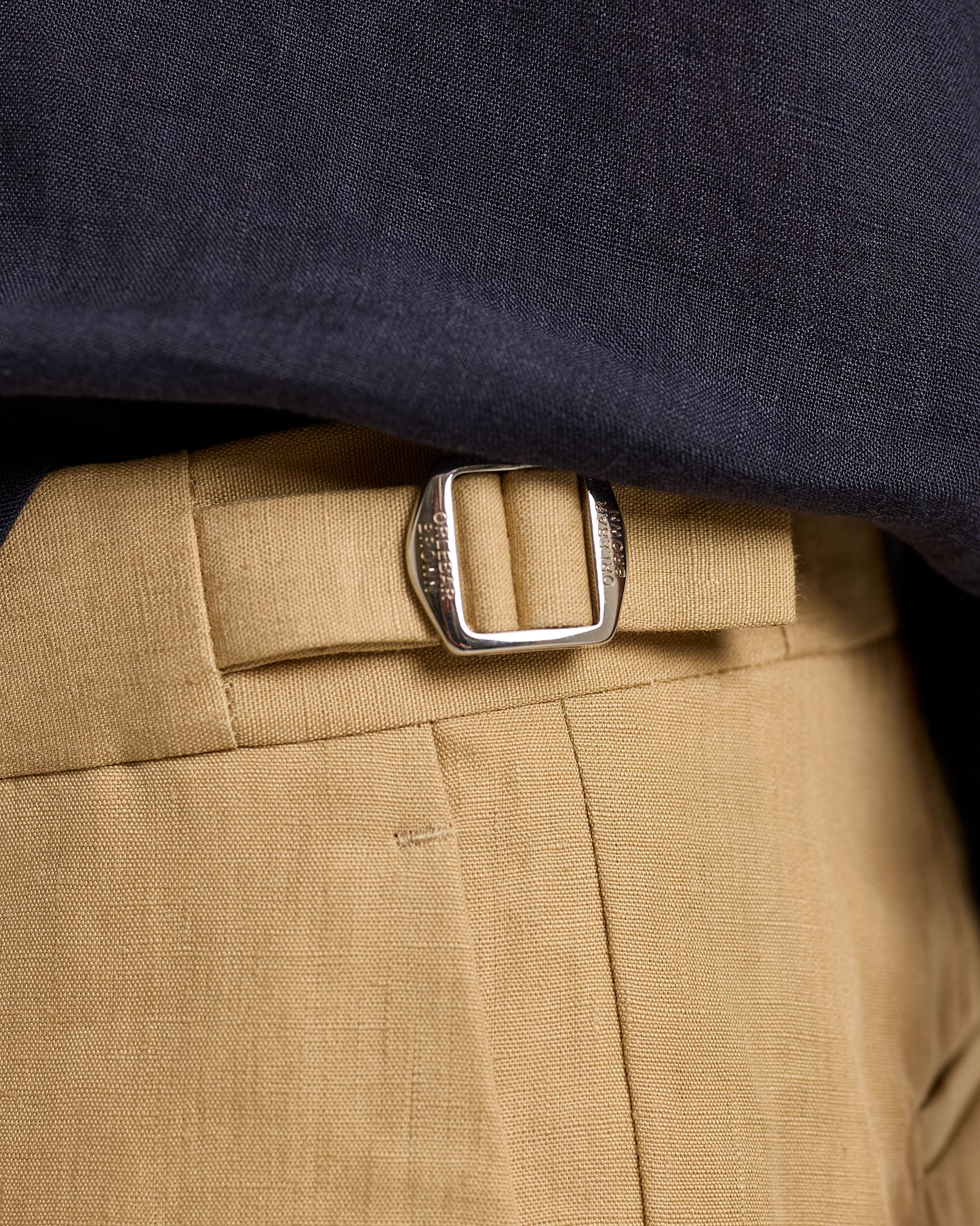 Close-up of beige pants with a silver buckle and navy shirt