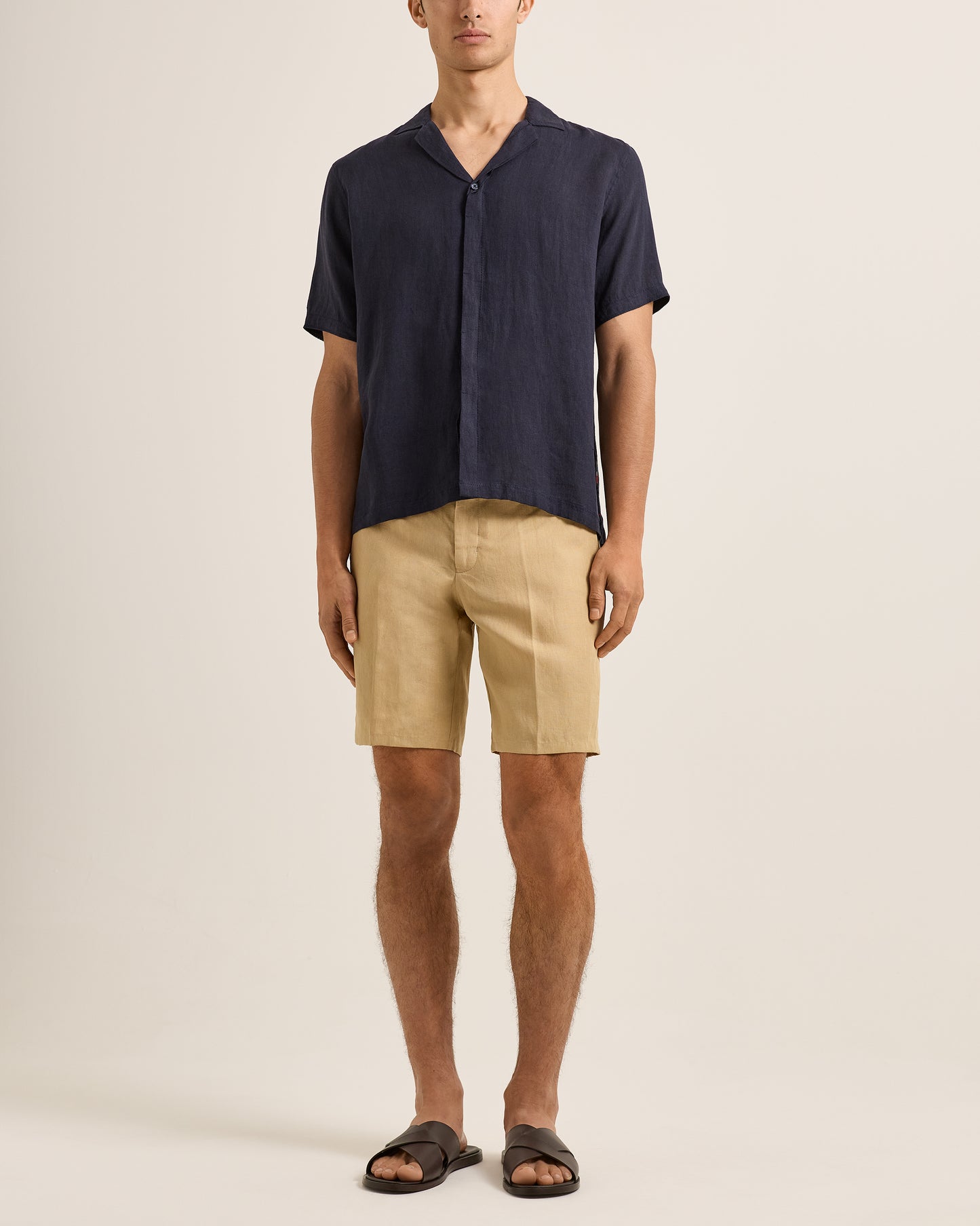 Person wearing a navy shirt and beige shorts on a plain background