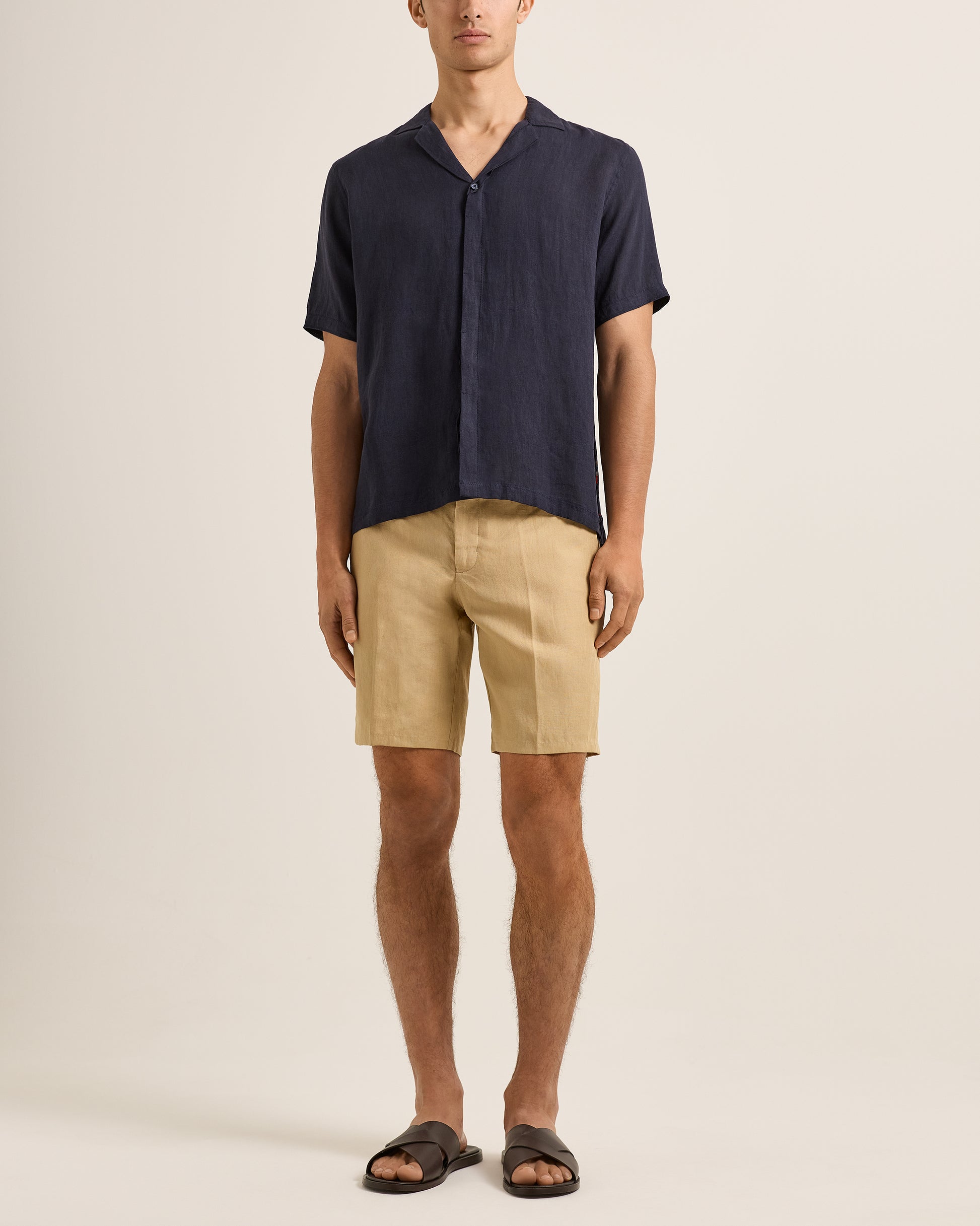 Person wearing a navy shirt and beige shorts on a plain background