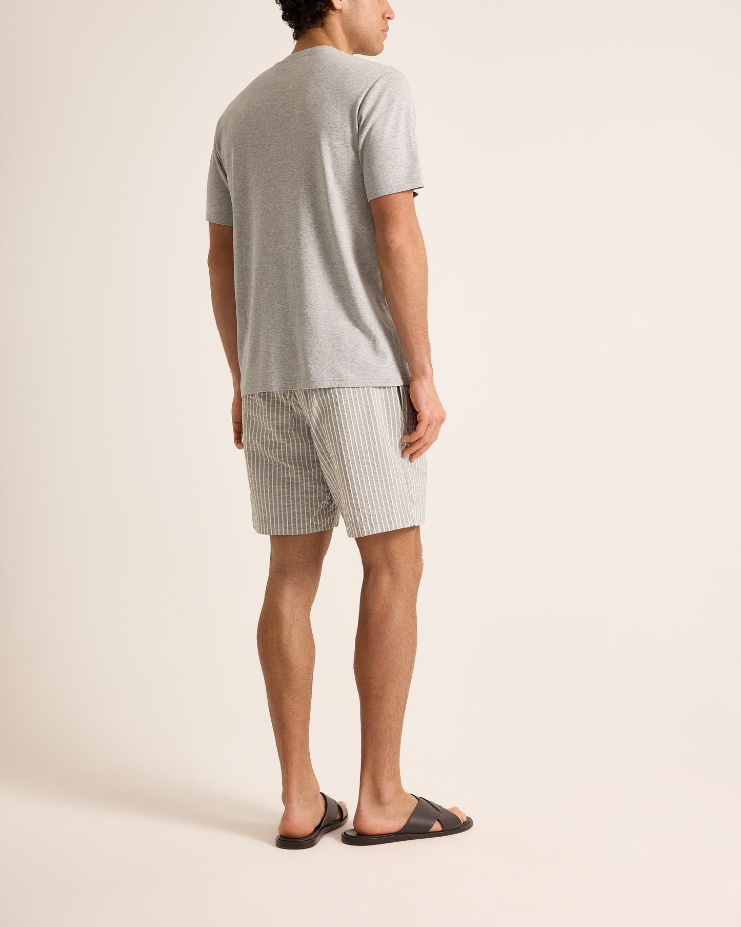 Man wearing a gray t-shirt and checkered shorts on a beige background