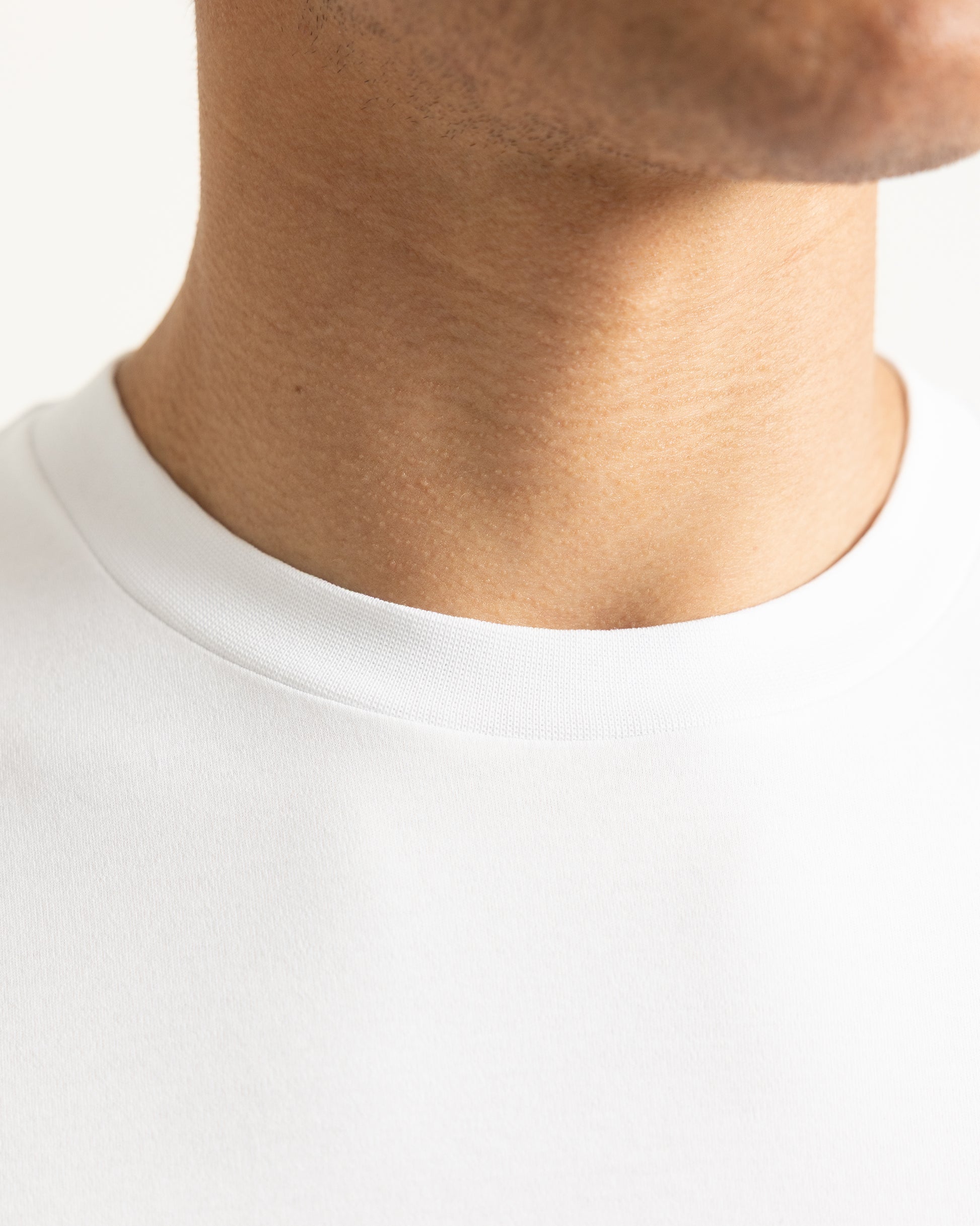 Close-up of a person's neck and lower face wearing a plain white crew-neck t-shirt against a light neutral background.