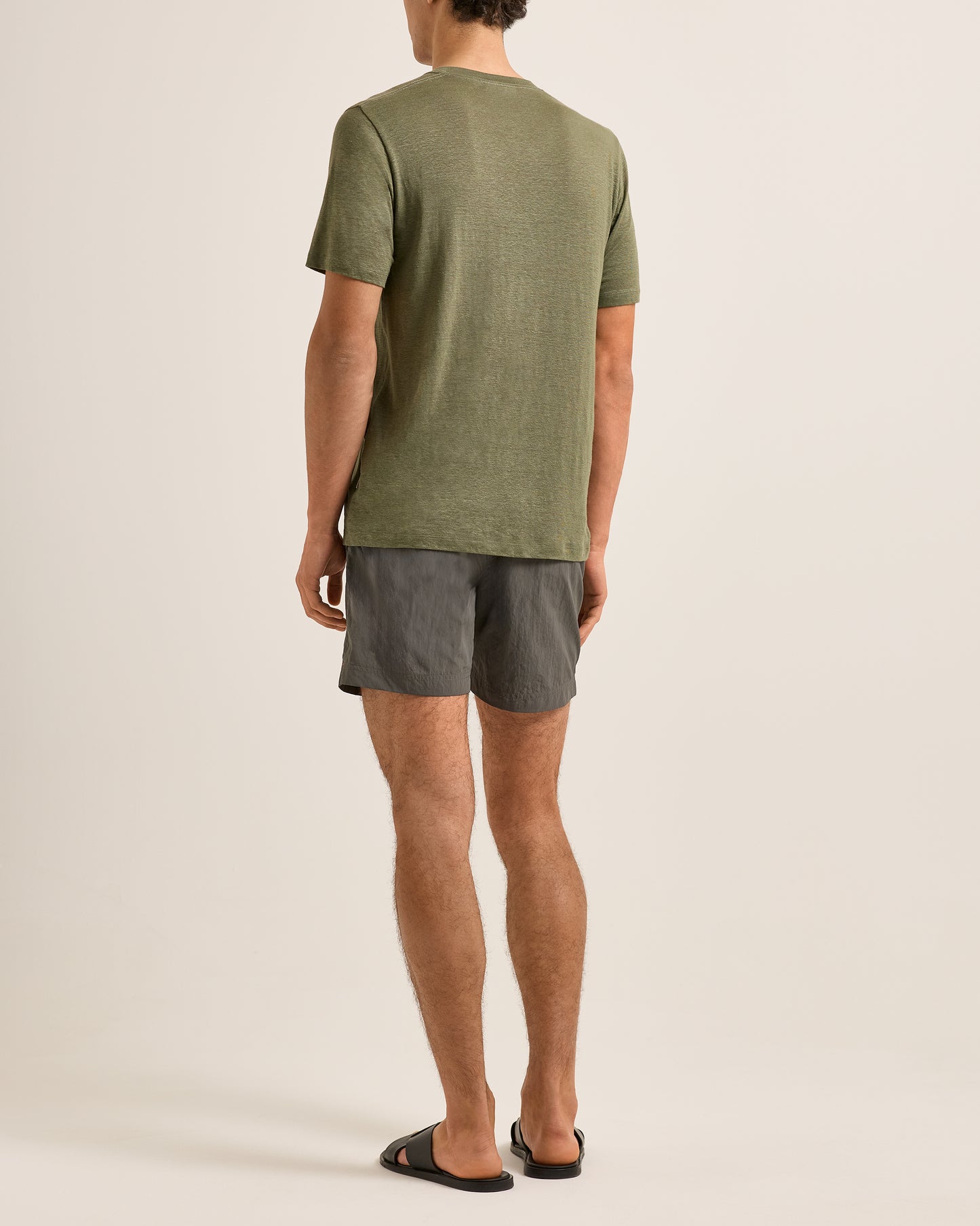 Person wearing a green t-shirt and gray shorts on a beige background