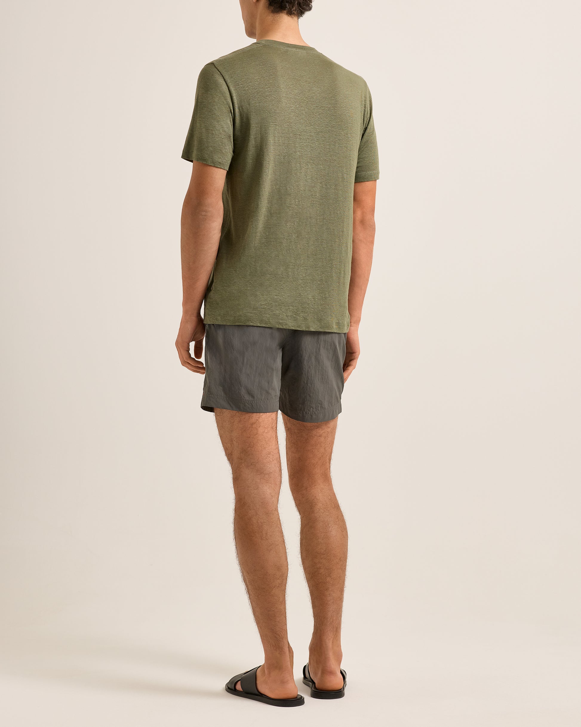 Person wearing a green t-shirt and gray shorts on a beige background