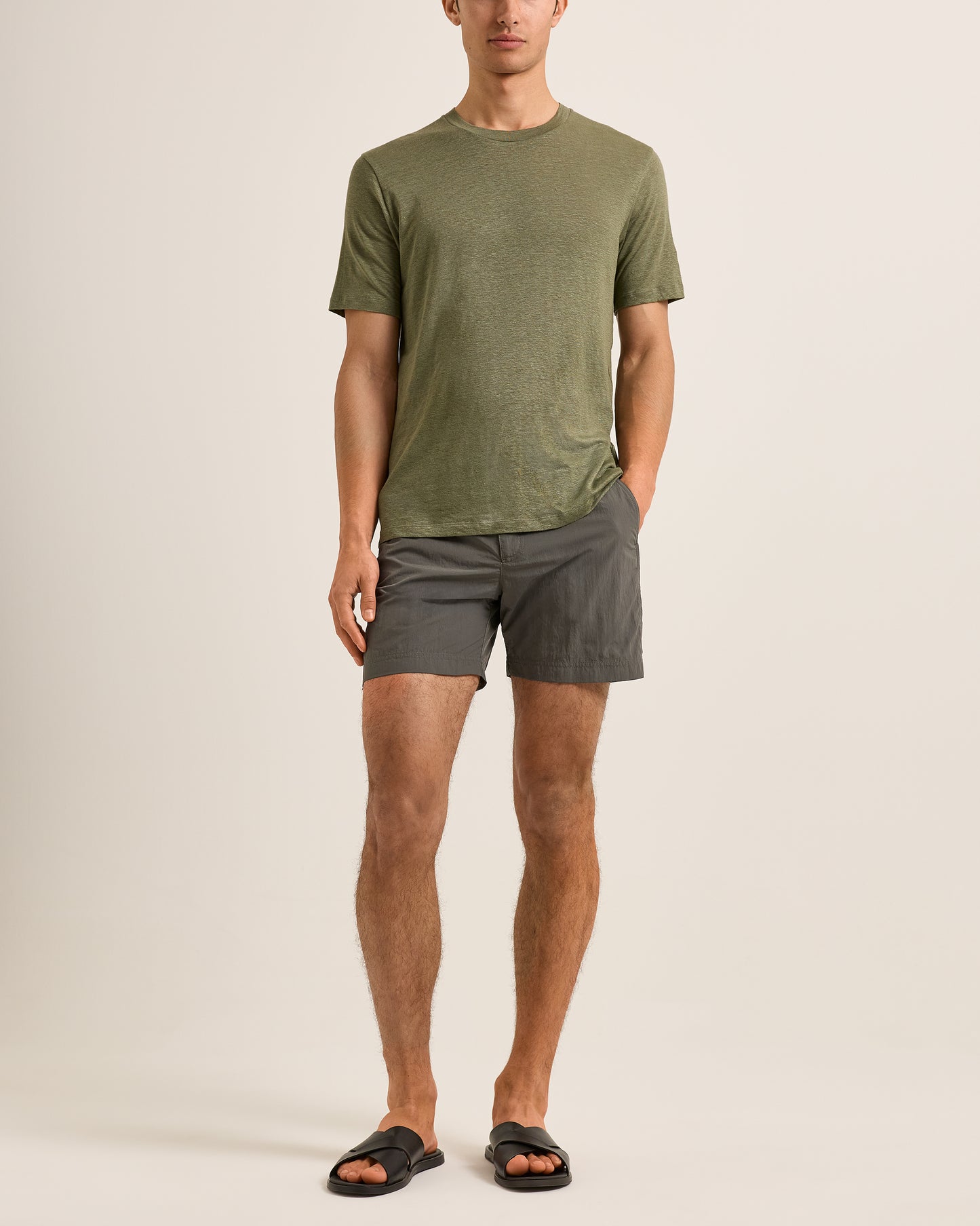Man wearing an olive green t-shirt and gray shorts on a beige background