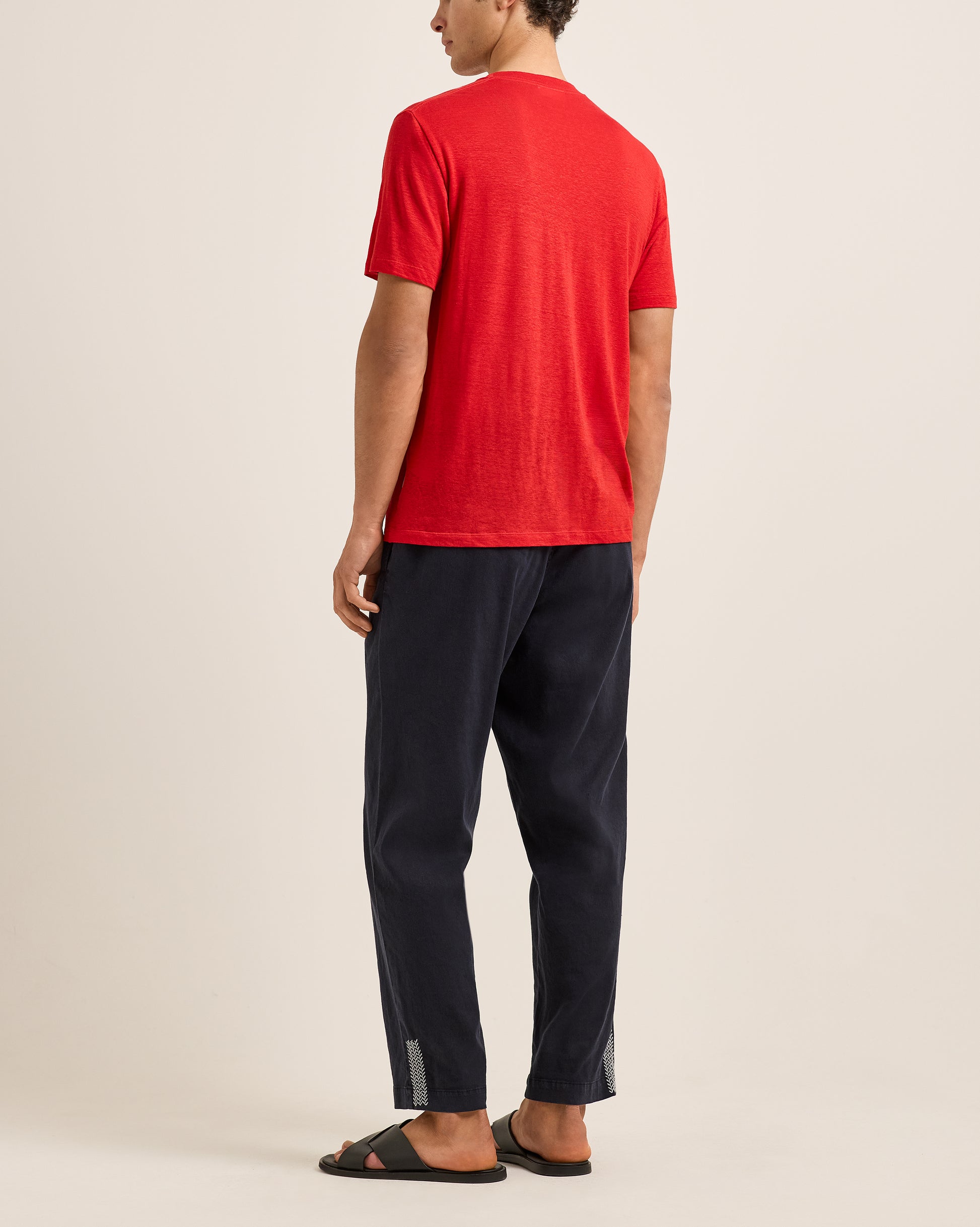 Person wearing a red t-shirt and black pants on a beige background