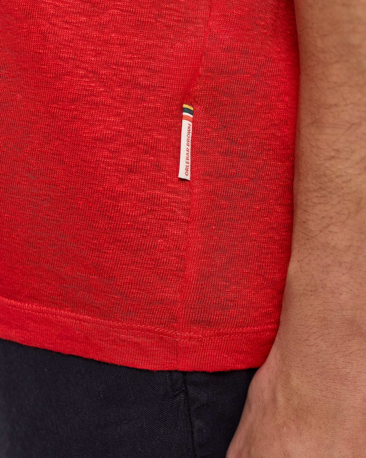 Close-up of a red shirt with a brand label on a person wearing black pants.