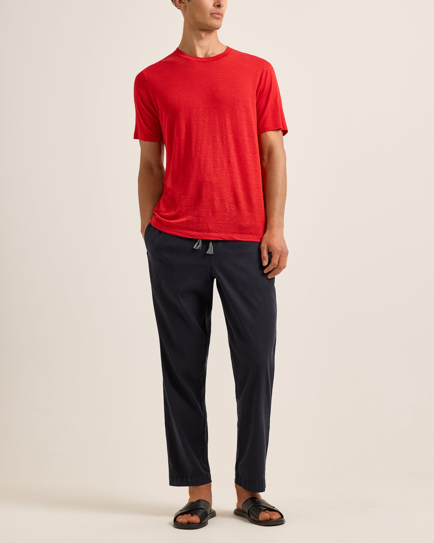 Person wearing a red t-shirt and black pants on a beige background