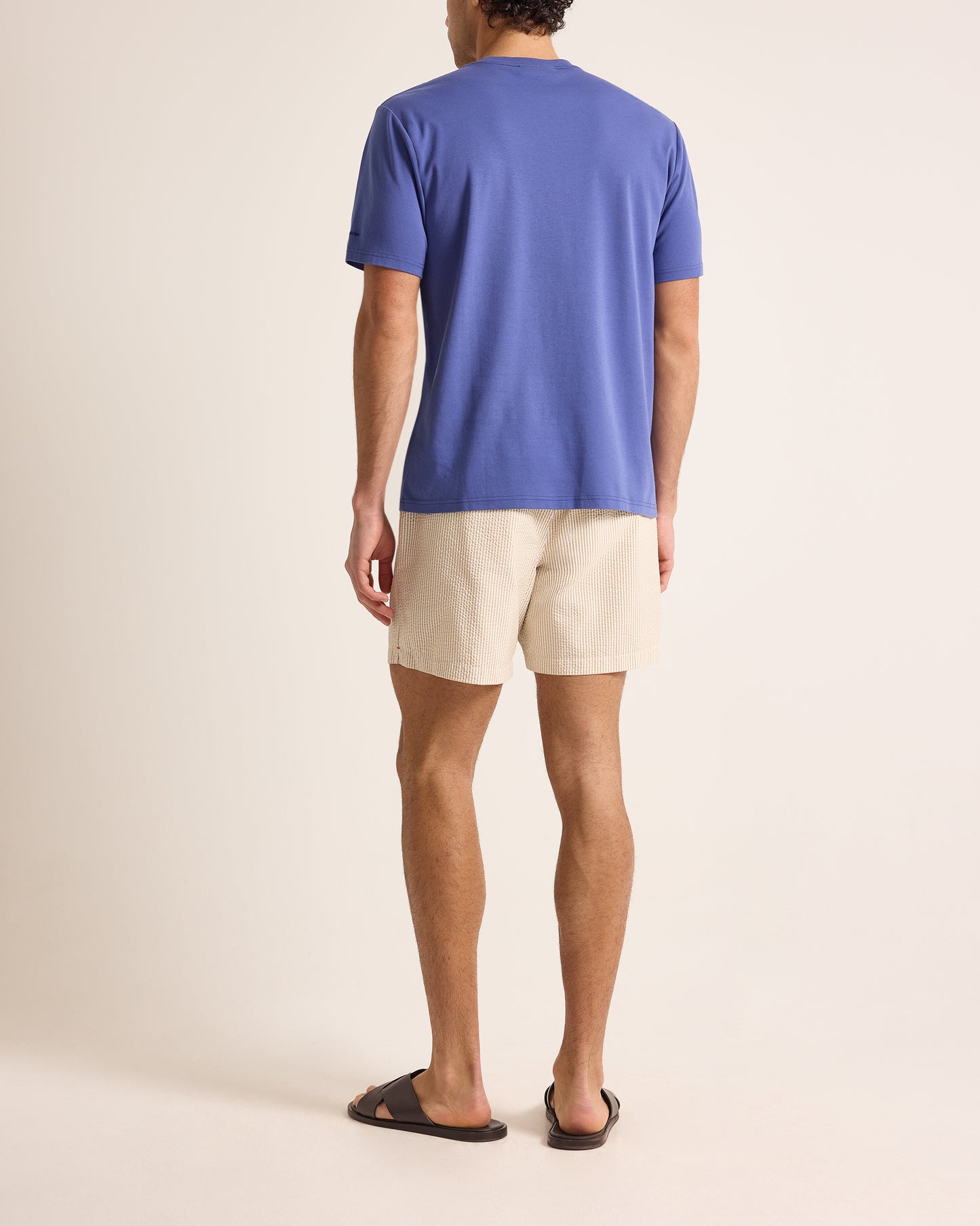 Man wearing a blue shirt and beige shorts on a plain background