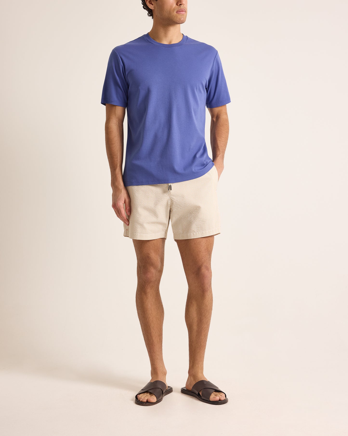 Man wearing a blue t-shirt and beige shorts on a plain background