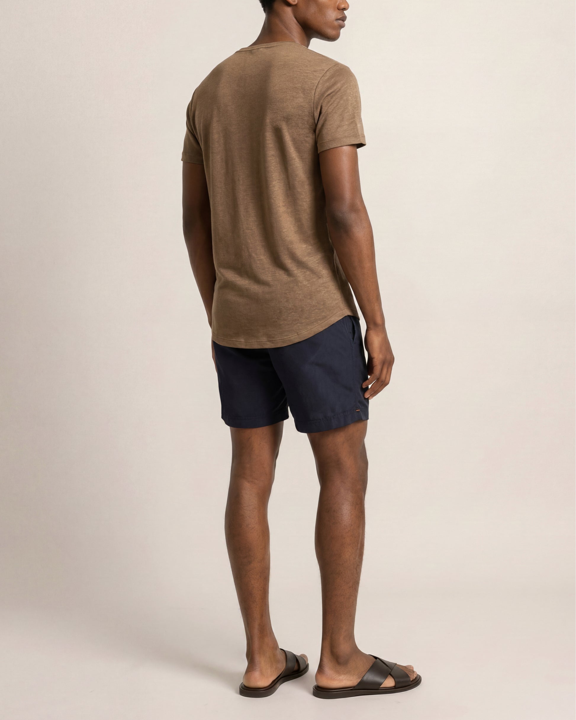 Man wearing a brown t-shirt and navy shorts on a beige background
