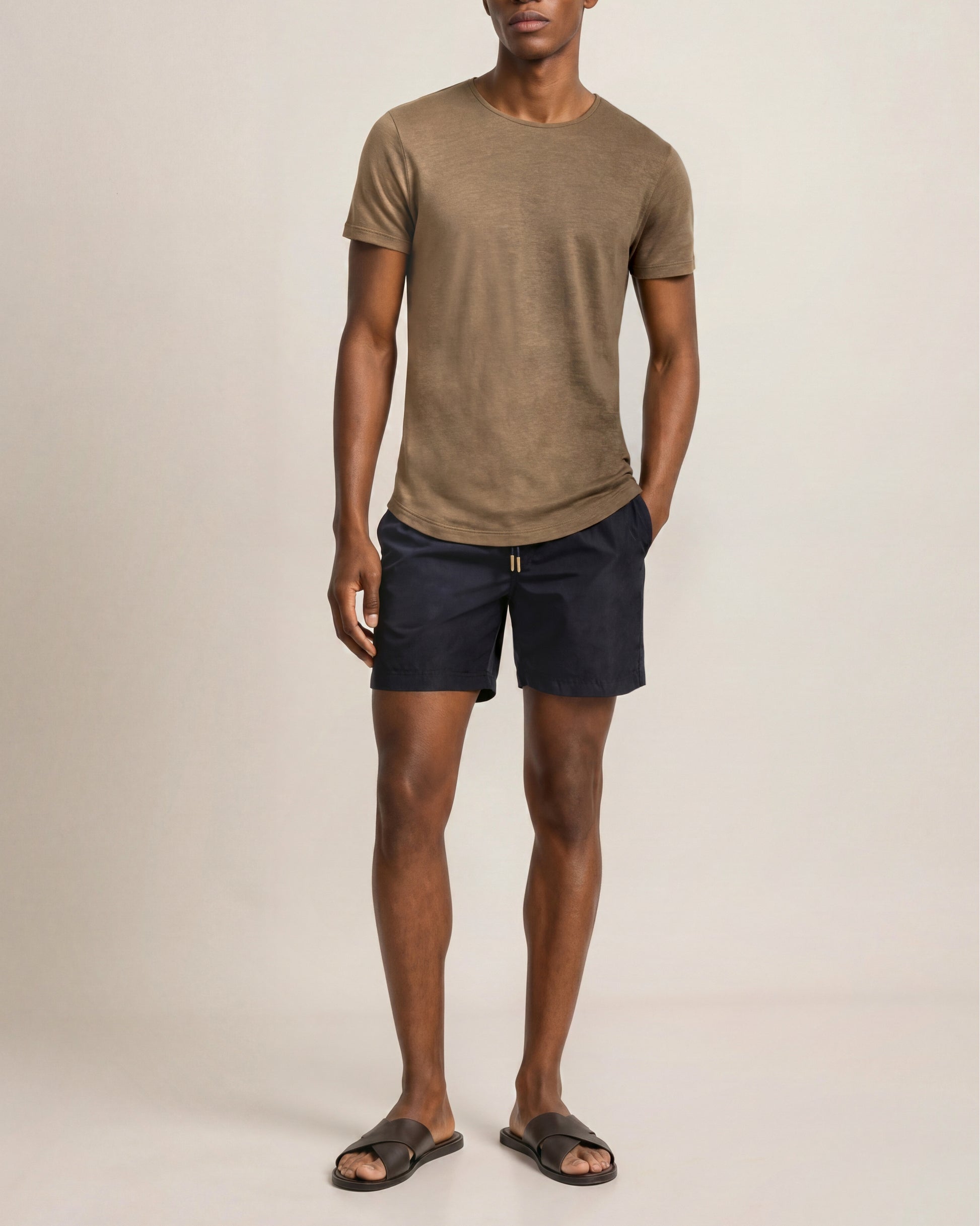 Man wearing a brown t-shirt and navy shorts on a beige background