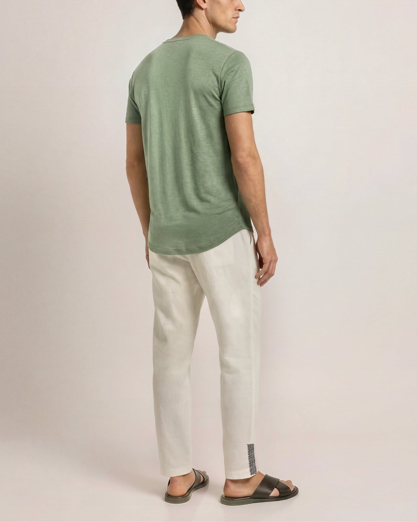 Man wearing a green t-shirt and white pants against a plain background