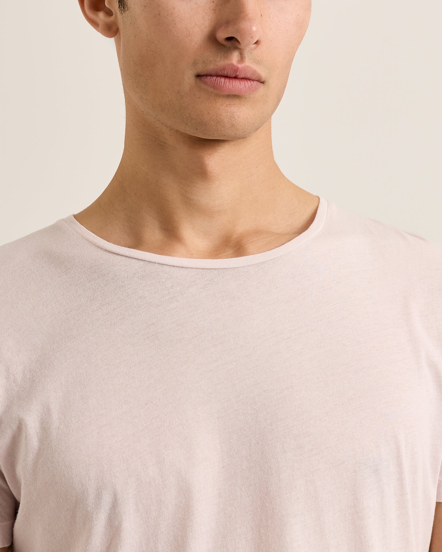 Close-up of a person wearing a light pink t-shirt against a neutral background