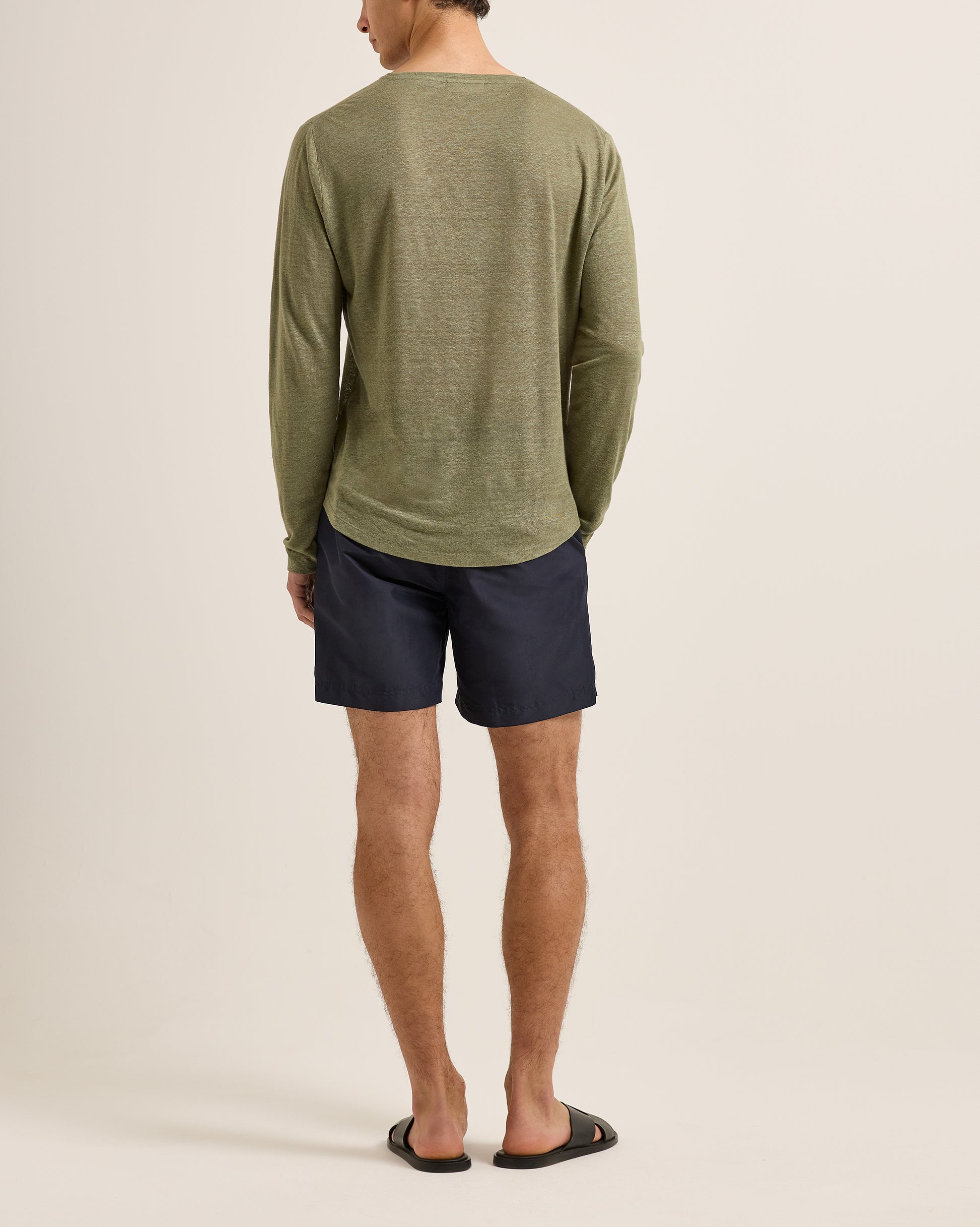 Person wearing a green long-sleeve shirt and navy shorts on a beige background