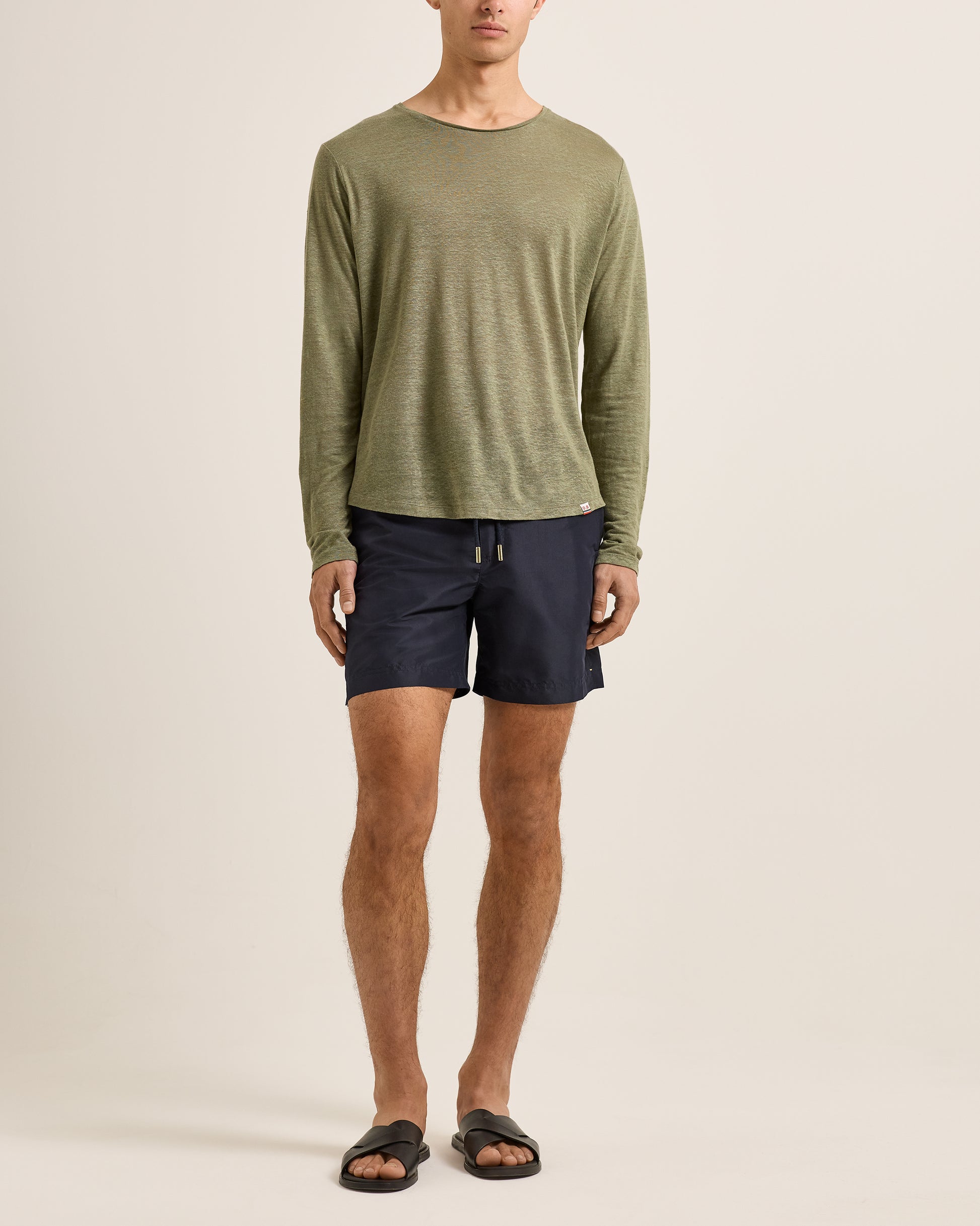 Person wearing a green long-sleeve shirt and navy shorts on a beige background