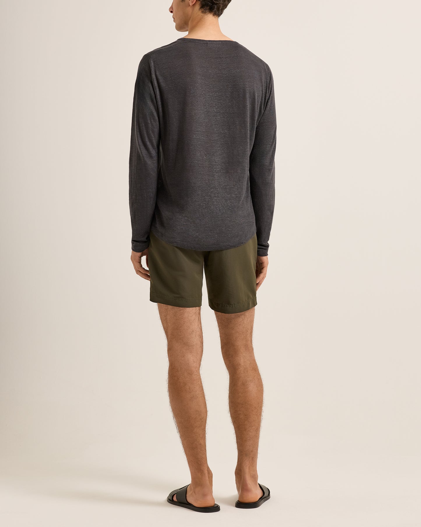Person wearing a dark gray long-sleeve shirt and green shorts on a beige background