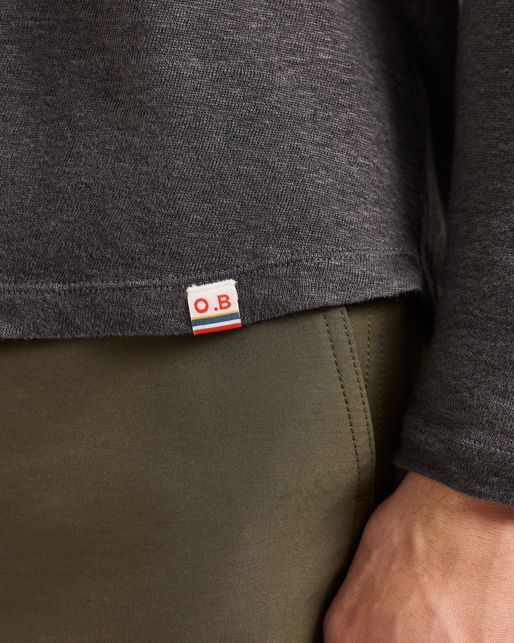 Close-up of a person wearing a dark gray long-sleeve shirt with a visible brand label, standing against a neutral background.