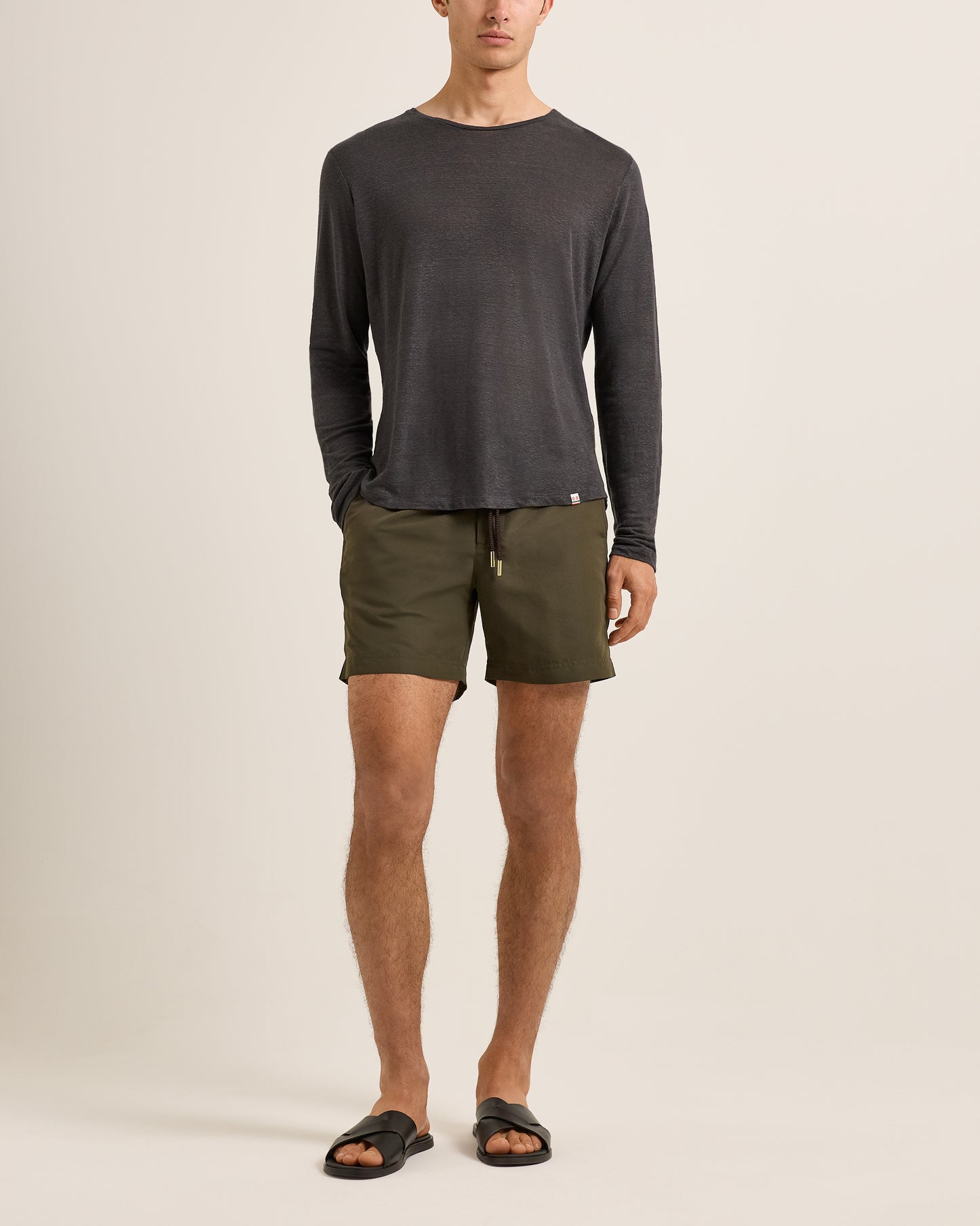 Person wearing a dark long-sleeve shirt and green shorts on a beige background