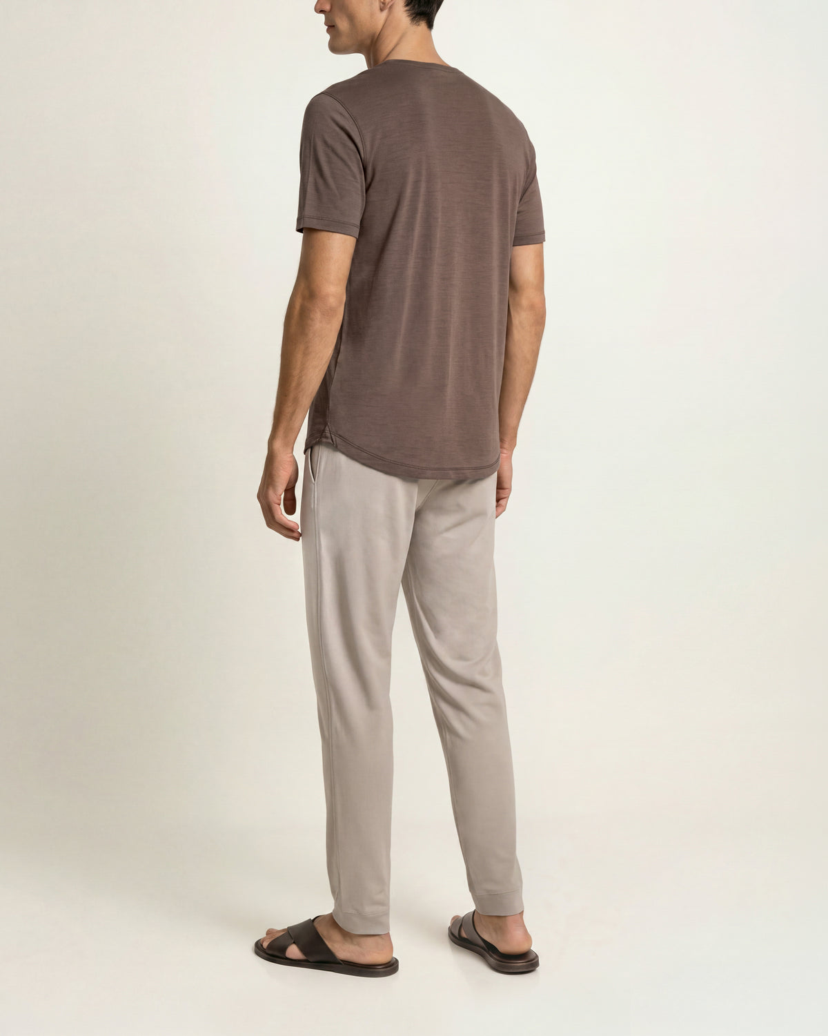 Man wearing brown relaxed fit t-short with beige sweatpants and brown sandals on a plain background