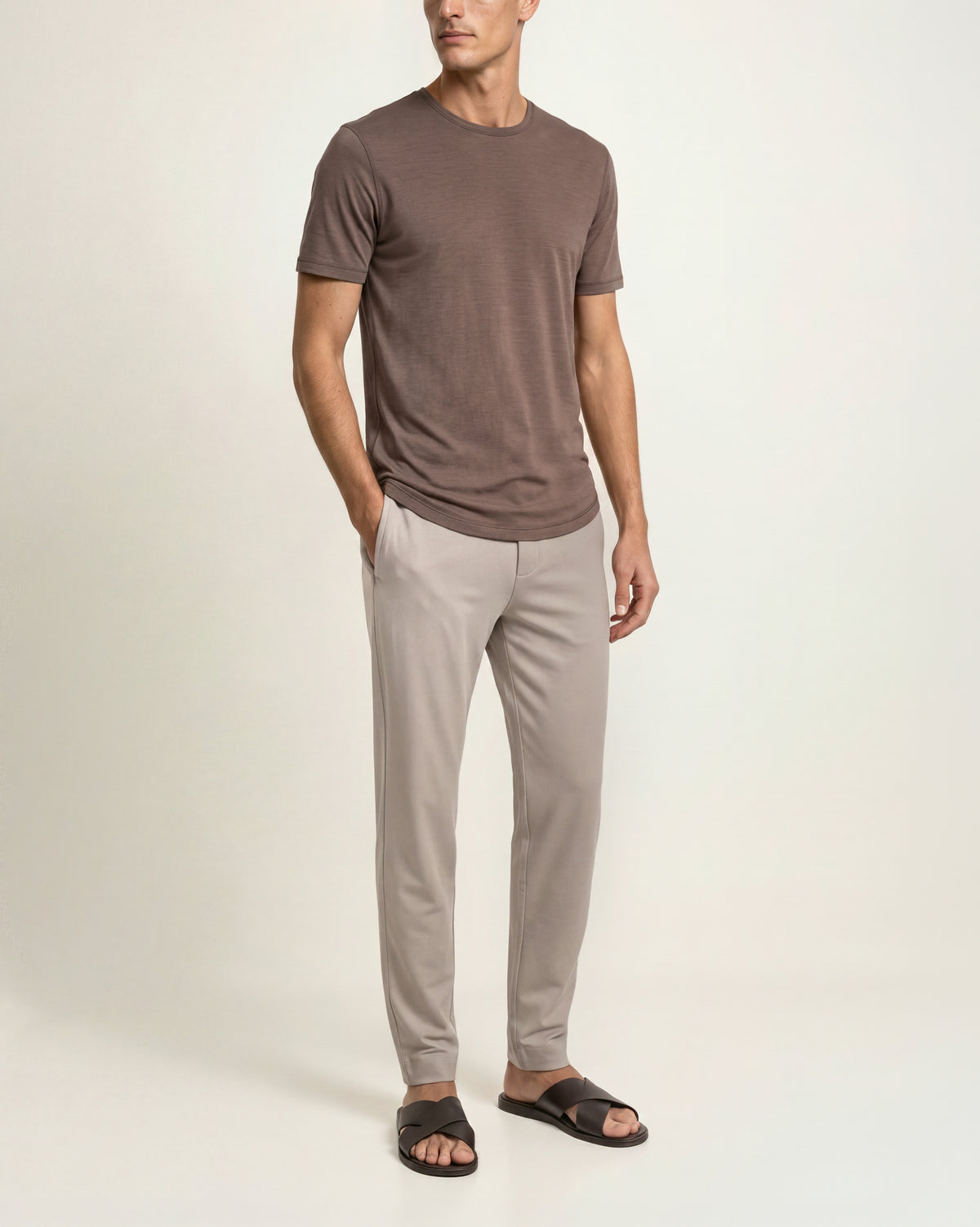 Man wearing brown t-shirt with beige sweatpants and brown sandals on a plain background