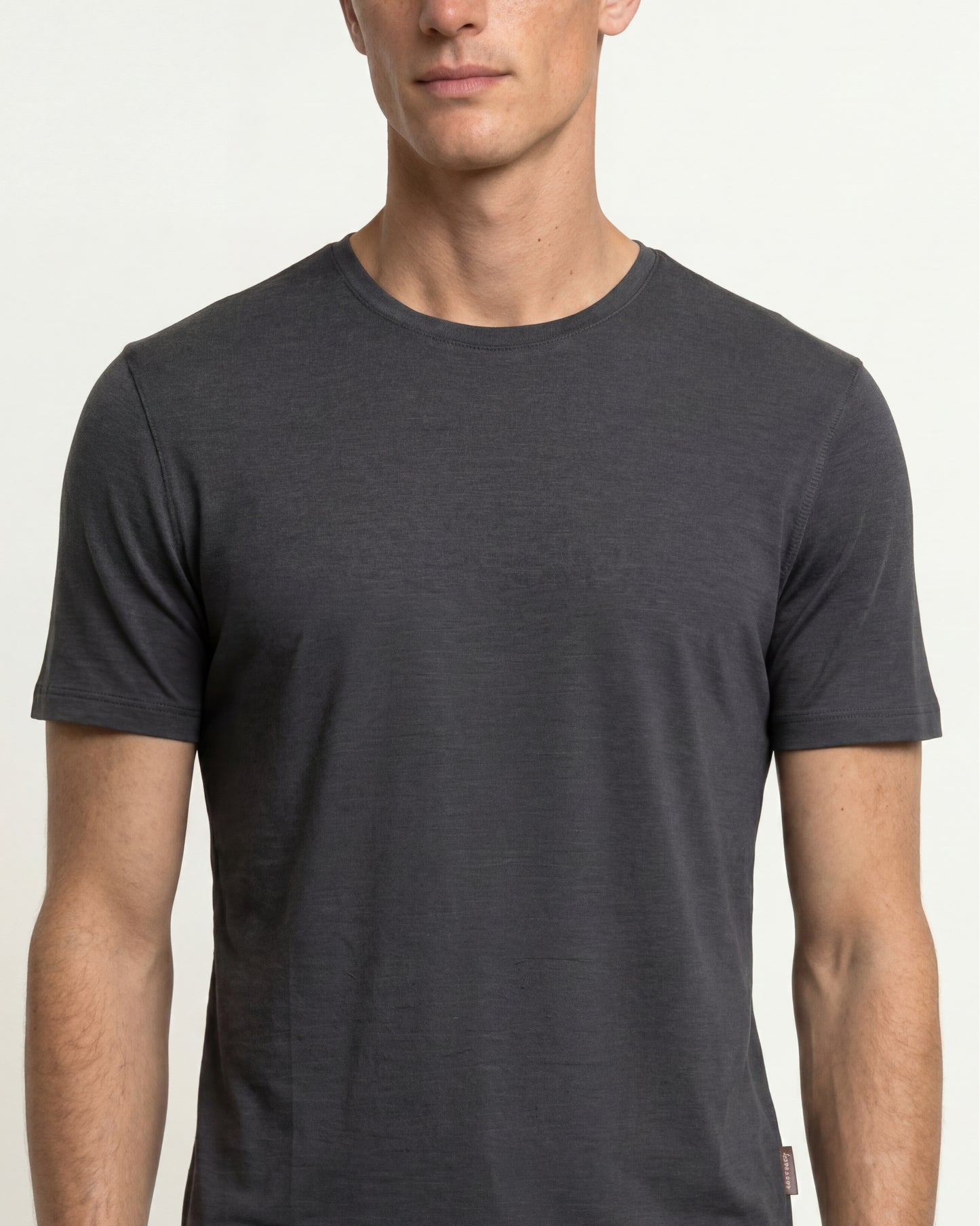 A man wearing a dark charcoal gray short-sleeve crewneck t-shirt, shown from the chest up against a light off-white background.