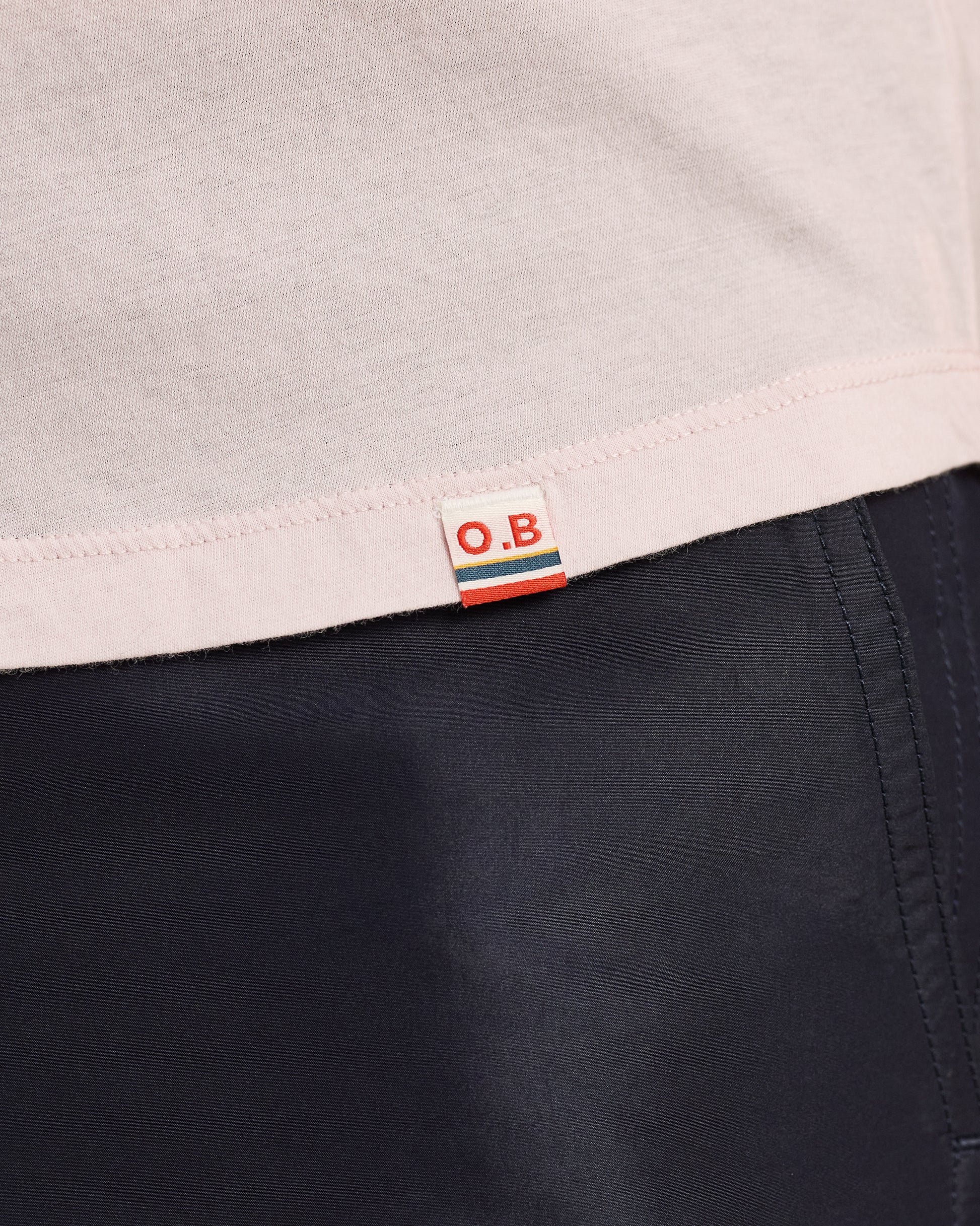 Close-up of a label with 'O.B.' on a garment with a light gray top and dark fabric.