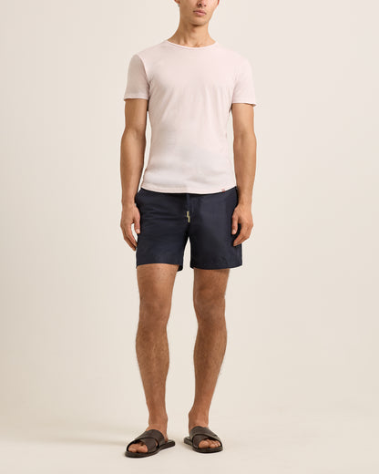 Person wearing a light pink t-shirt and navy shorts on a plain background