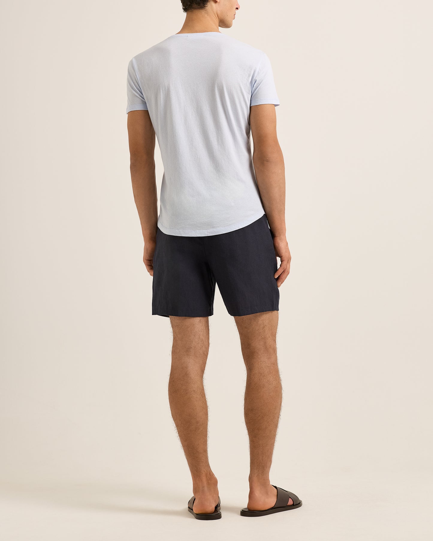 Man wearing a blue t-shirt and dark shorts on a beige background