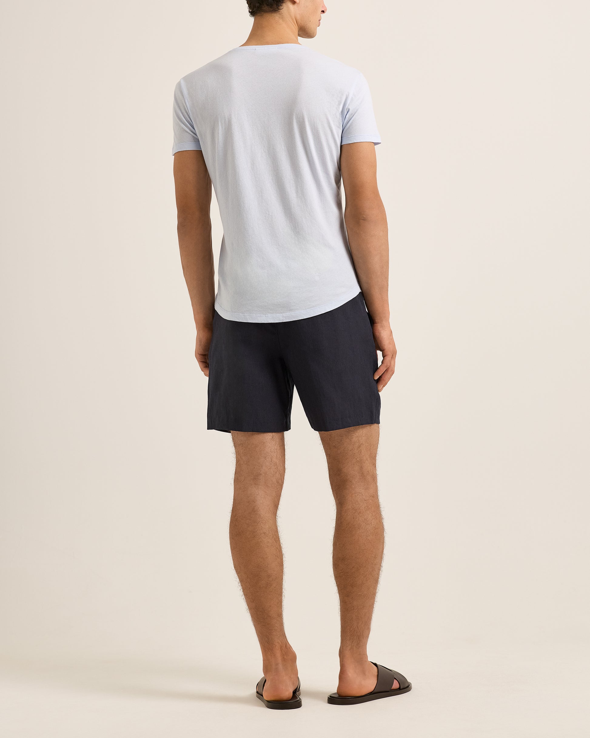 Man wearing a blue t-shirt and dark shorts on a beige background