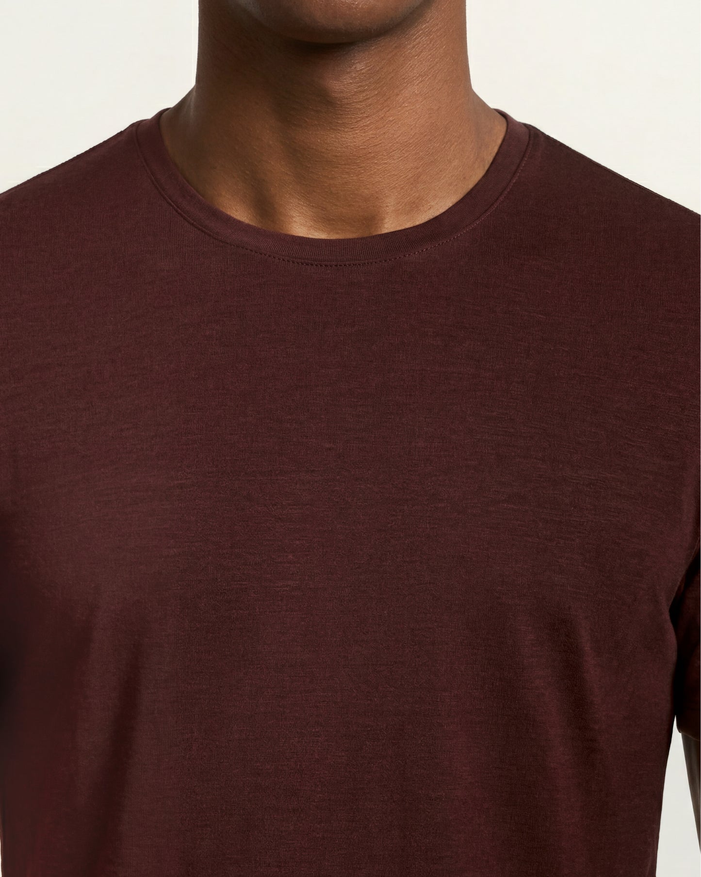 A close-up of a person wearing a crew-neck t-shirt in a dark burgundy or maroon color, shown against a plain light background.
