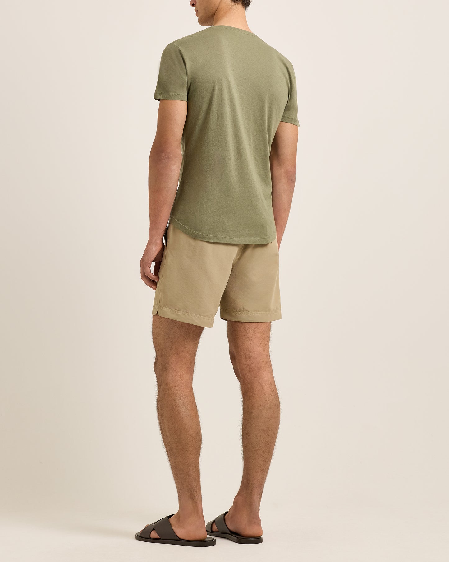 Man wearing a green t-shirt and beige shorts on a plain background