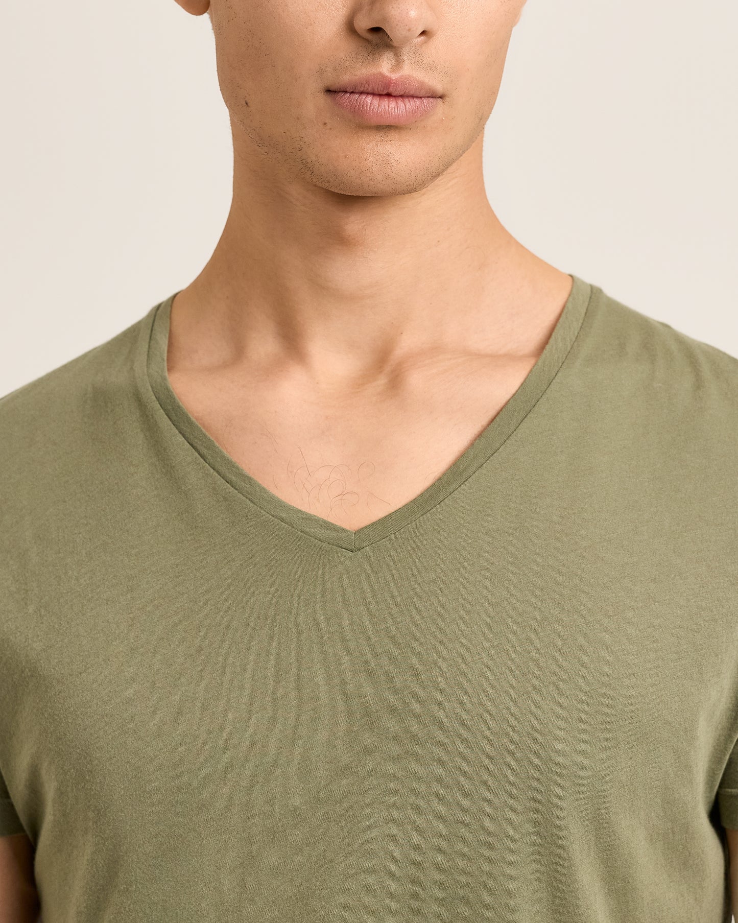 Close-up of a person wearing an olive green V-neck shirt against a neutral background