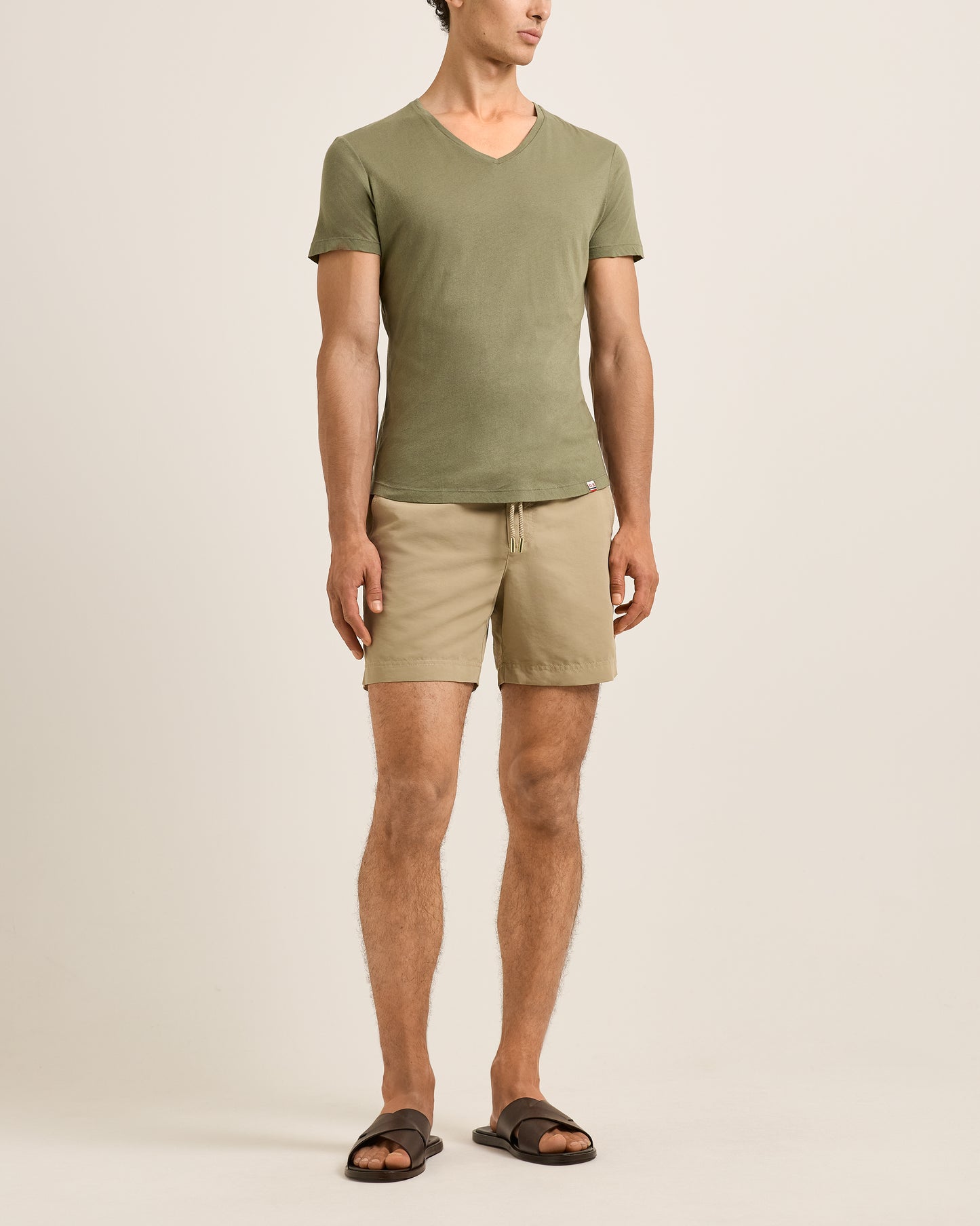 Person wearing a green t-shirt and beige shorts on a plain background